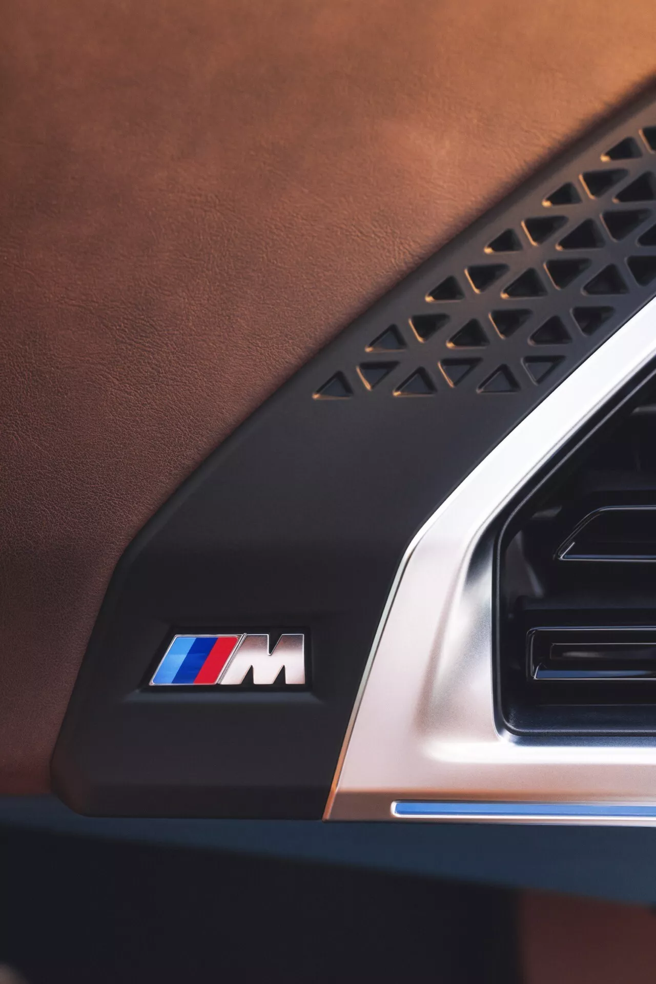 Close-up view of BMW XM 2023 (G09) interior showing leather upholstery, geometric patterned element, M emblem with iconic stripes, and metallic air vent detail
