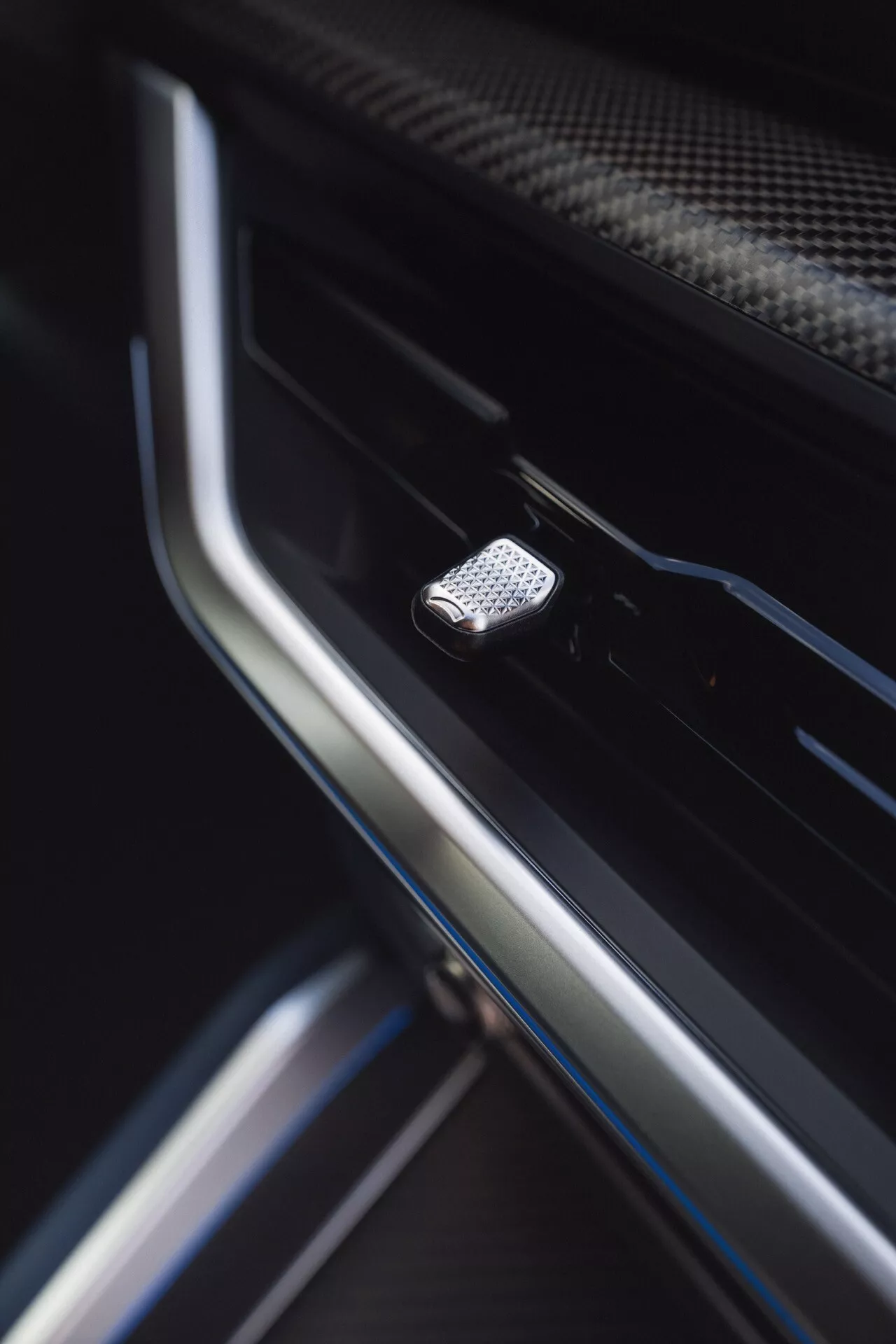 Close-up view of a high-texture metallic button in the door interior of a 2023 BMW XM (G09), with shallow depth of field emphasizing its design and surrounding luxury materials