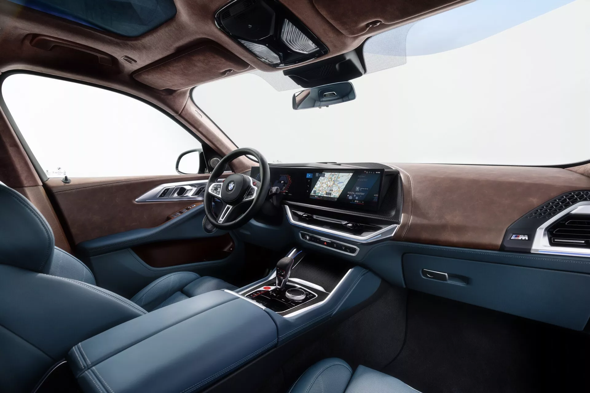Close-up view of the 2023 BMW XM (G09) interior showing the driver's seat, modern dashboard with digital gauges, infotainment touchscreen, and luxurious center console from the rear seat perspective