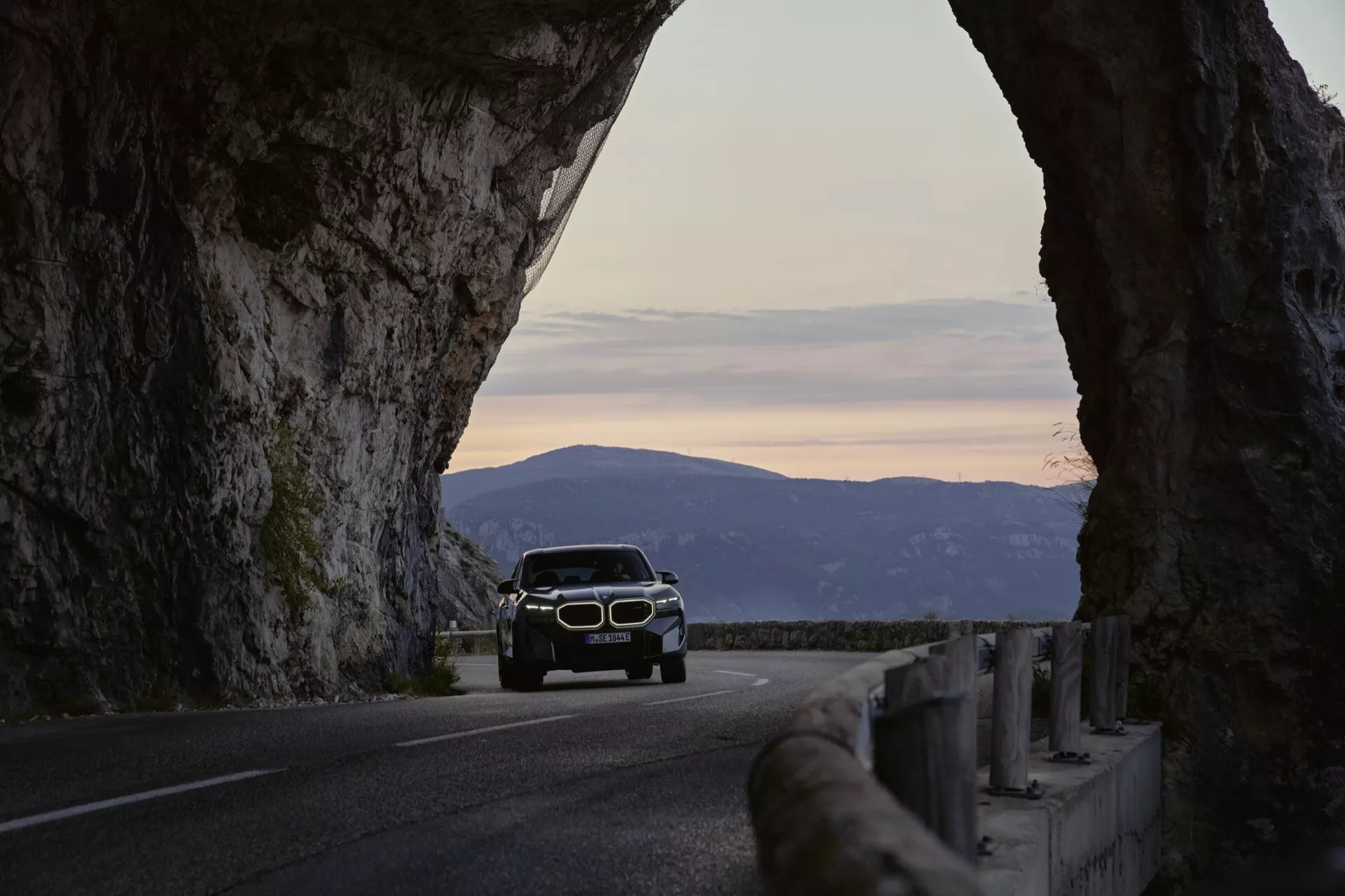 2023 BMW XM (G09) positioned on a scenic mountain road at sunrise, emphasizing the natural landscape and adventurous driving experience
