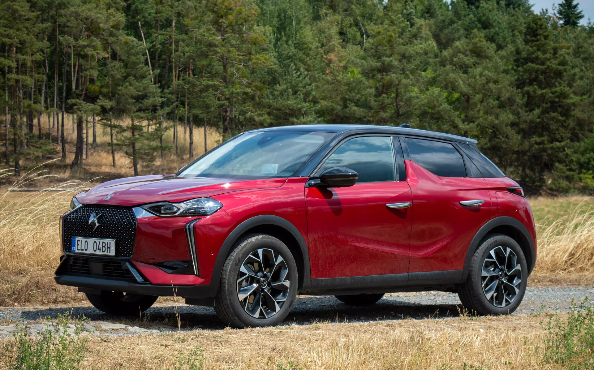 2023 DS Automobiles DS 3 E-TENSE Side-Front View, Red Crossover SUV, Multi-Spoke Alloy Wheels, LED Headlights, on Gravel Path with Forest Background