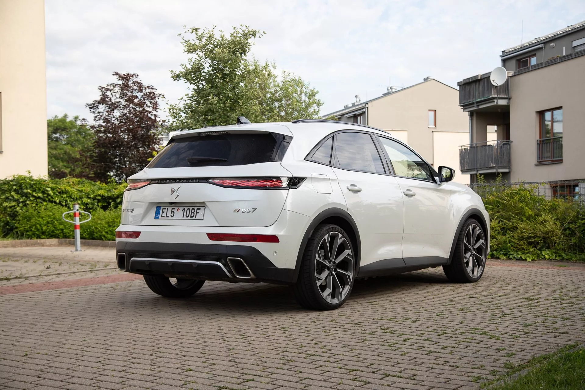 Rear three-quarter view of a DS Automobiles DS 7 2022 in white, showcasing side profile and rear with distinctive slim horizontal taillights, badging, high-mounted spoiler, shark-fin antenna, parking sensors, dual exhaust system, and large multi-spoke alloy wheels on a residential street.
