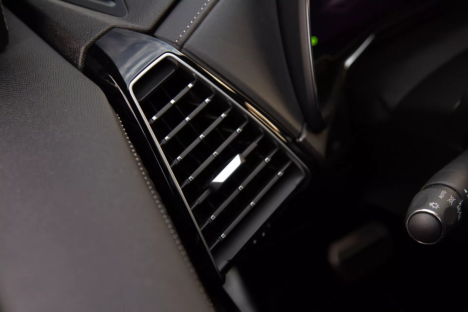 Close-up view of the DS Automobiles DS-7 2022 air vent on the dashboard with vertically aligned black adjustable slats, glossy bezel, and a silver accent on the control, showcasing the vehicle's interior design quality and materials