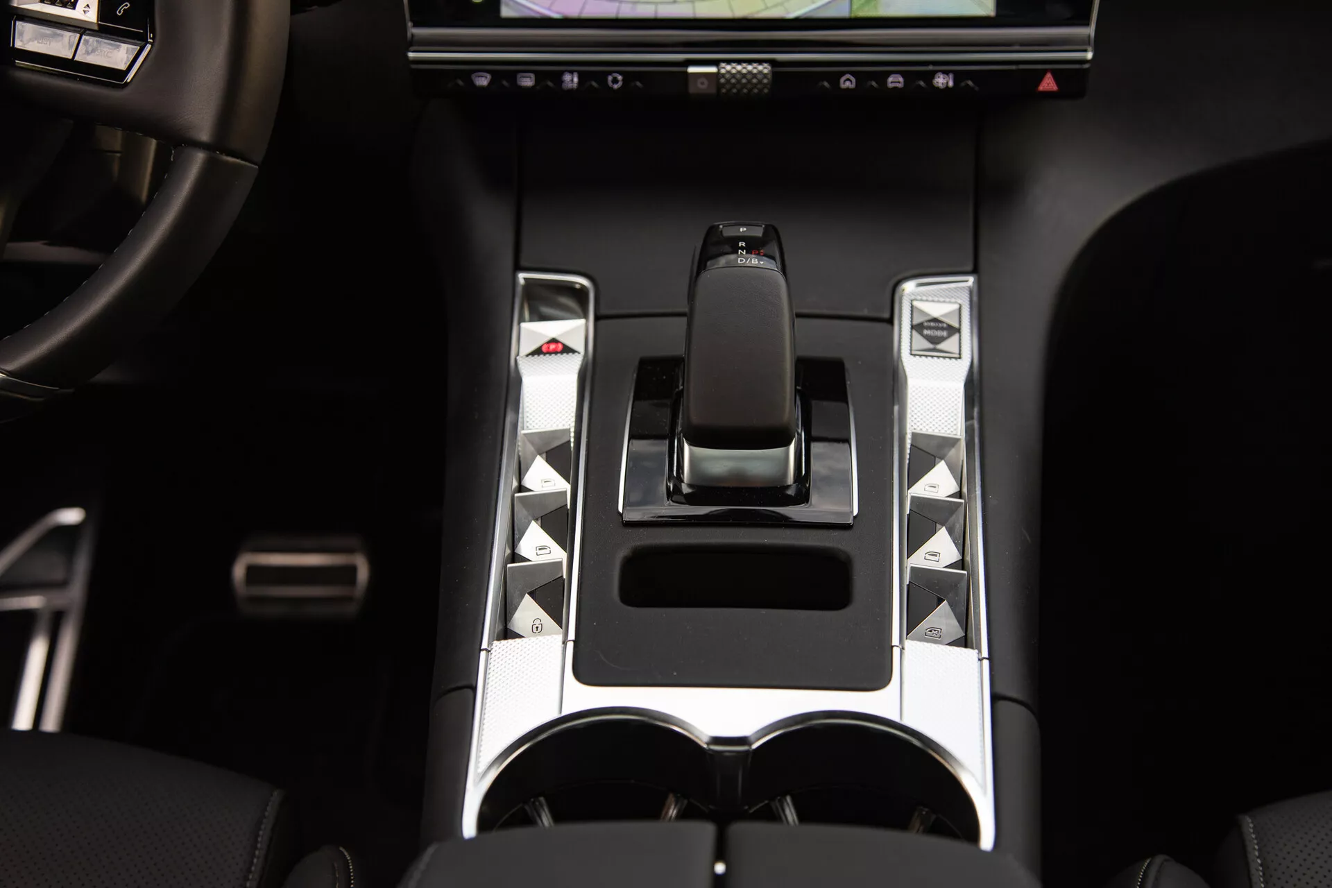 Detailed view of the DS Automobiles DS-7 2022 center console featuring an ergonomic gear shift, metallic accents, unique control buttons, touchscreen display, and dual cup holders, highlighting advanced vehicle control and luxury design elements.