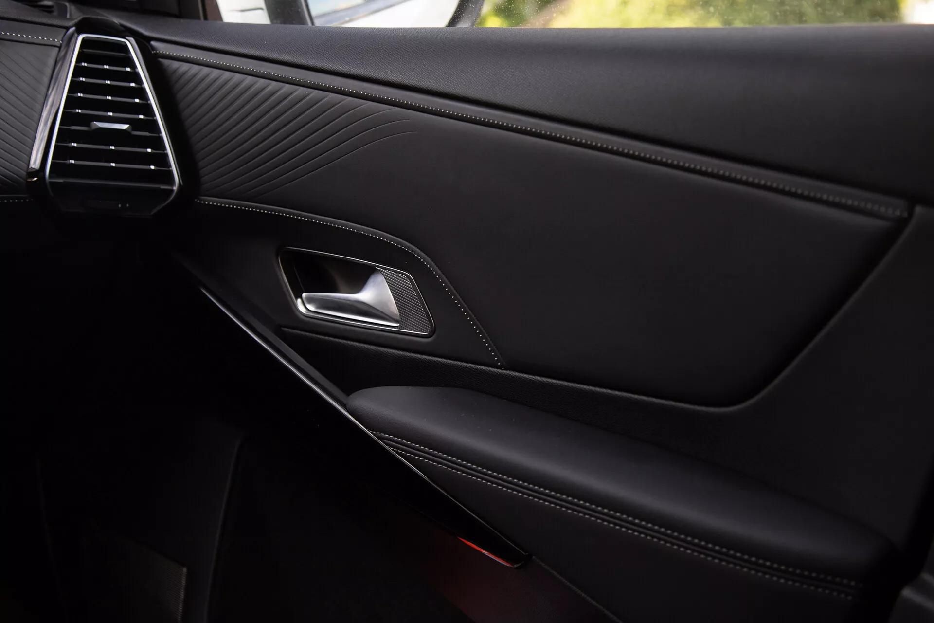 Close-up view of the DS Automobiles DS-7 2022 interior door panel showcasing the sleek air vent, stitched leather texture, chrome door handle, ergonomic latch lever, contrast-stitched armrest, and integrated storage pocket with a partially visible speaker grille, reflecting premium quality and design details.