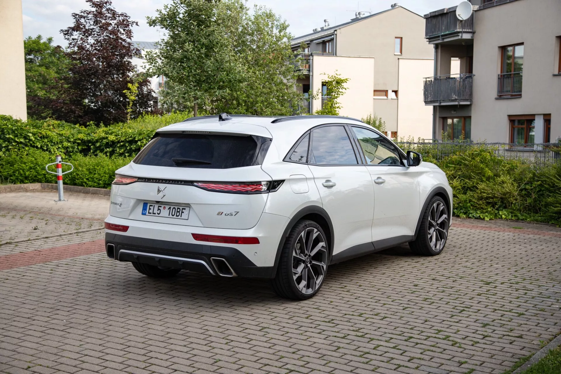 2022 DS Automobiles DS-7 white SUV parked on brick-paved area, showcasing LED taillights, a dual exhaust system, and sporty alloy wheels. The image captures the vehicle's sleek, coupe-like SUV design from a three-quarter rear perspective, highlighting a possible panoramic sunroof and technology-enhanced wing mirrors.