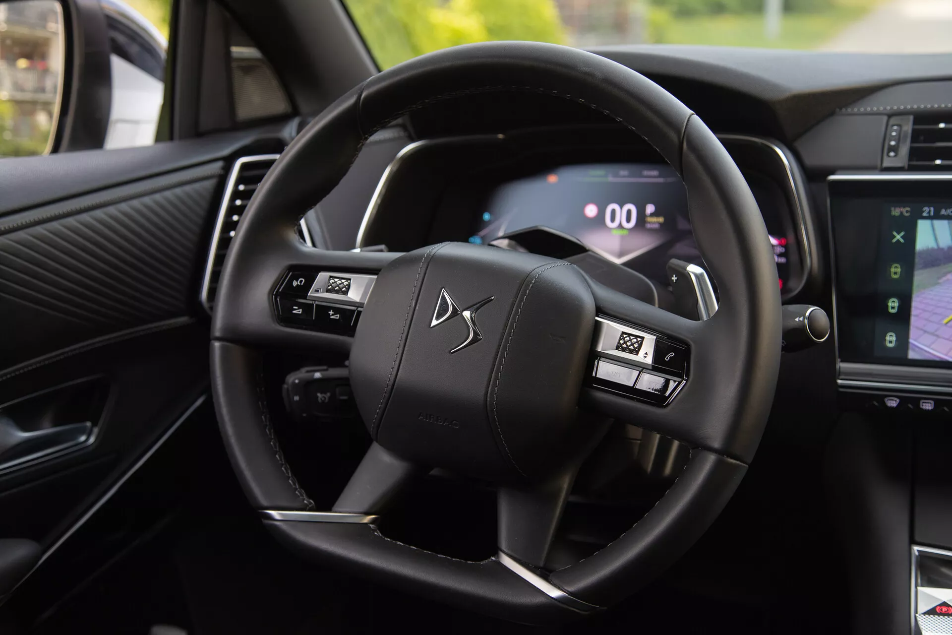 Interior view of the DS Automobiles DS-7 2022 displaying the steering wheel with multifunctional buttons and digital instrument cluster, including paddle shifters and part of the infotainment system showing navigation