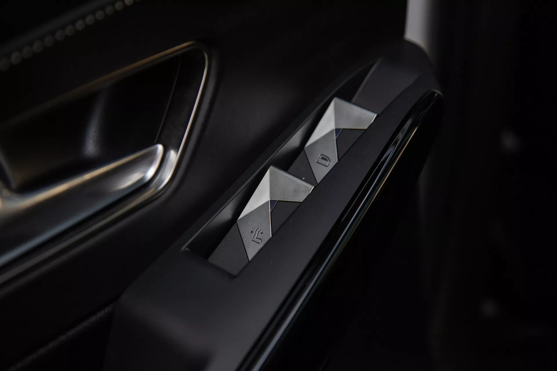 Close-up view of the DS Automobiles DS-7 2022 driver's side door controls, featuring diamond-cut window switches, door lock button, premium matte and metallic finishes, and sophisticated lighting highlighting the ergonomic design.