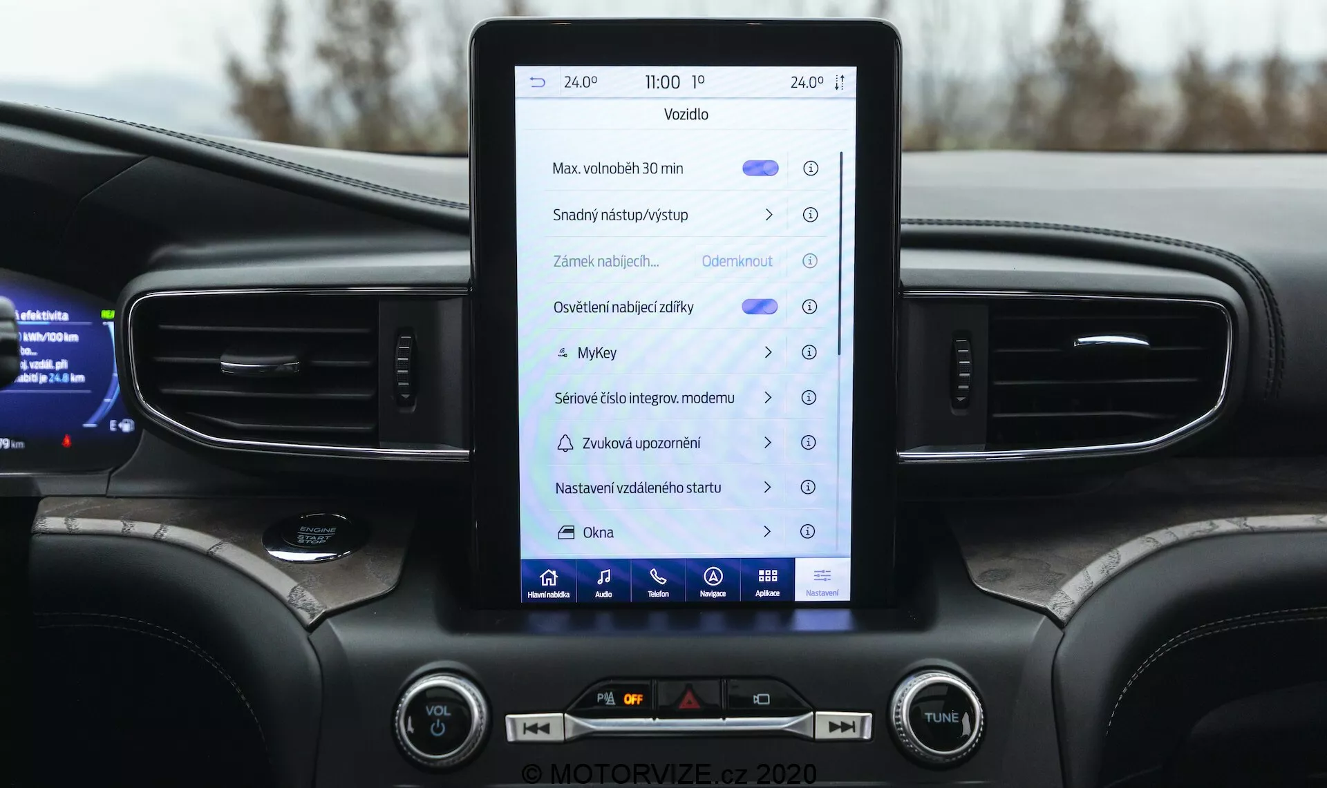 Close-up view of the 2019 Ford Explorer interior focusing on the center console and infotainment system. The vertically-oriented touchscreen displays icons and texts, suggesting features like navigation, vehicle settings, media controls, Bluetooth, and possibly Apple CarPlay or Android Auto. The dashboard includes vertical air vents, ambient lighting, physical buttons, and knobs for climate and audio control. The top of a multifunctional steering wheel and a partial digital instrument cluster displaying vehicle information are also visible. The design highlights a modern, mid-range or premium vehicle with a dark color scheme.
