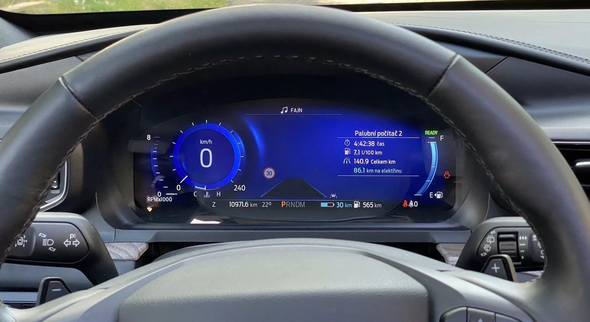Interior view of a 2019 Ford Explorer from the driver's seat perspective, focusing on the centrally positioned steering wheel and the digital dashboard behind it. The steering wheel features various control buttons on both spokes. Behind it, a fully digital instrument cluster displays information including speed, power gauge, driving range, fuel level, outside temperature, and efficiency reading. The dashboard also shows time and date, and is designed with modern, technologically advanced elements in blue and white. The steering wheel is made of black leather with stitching details.