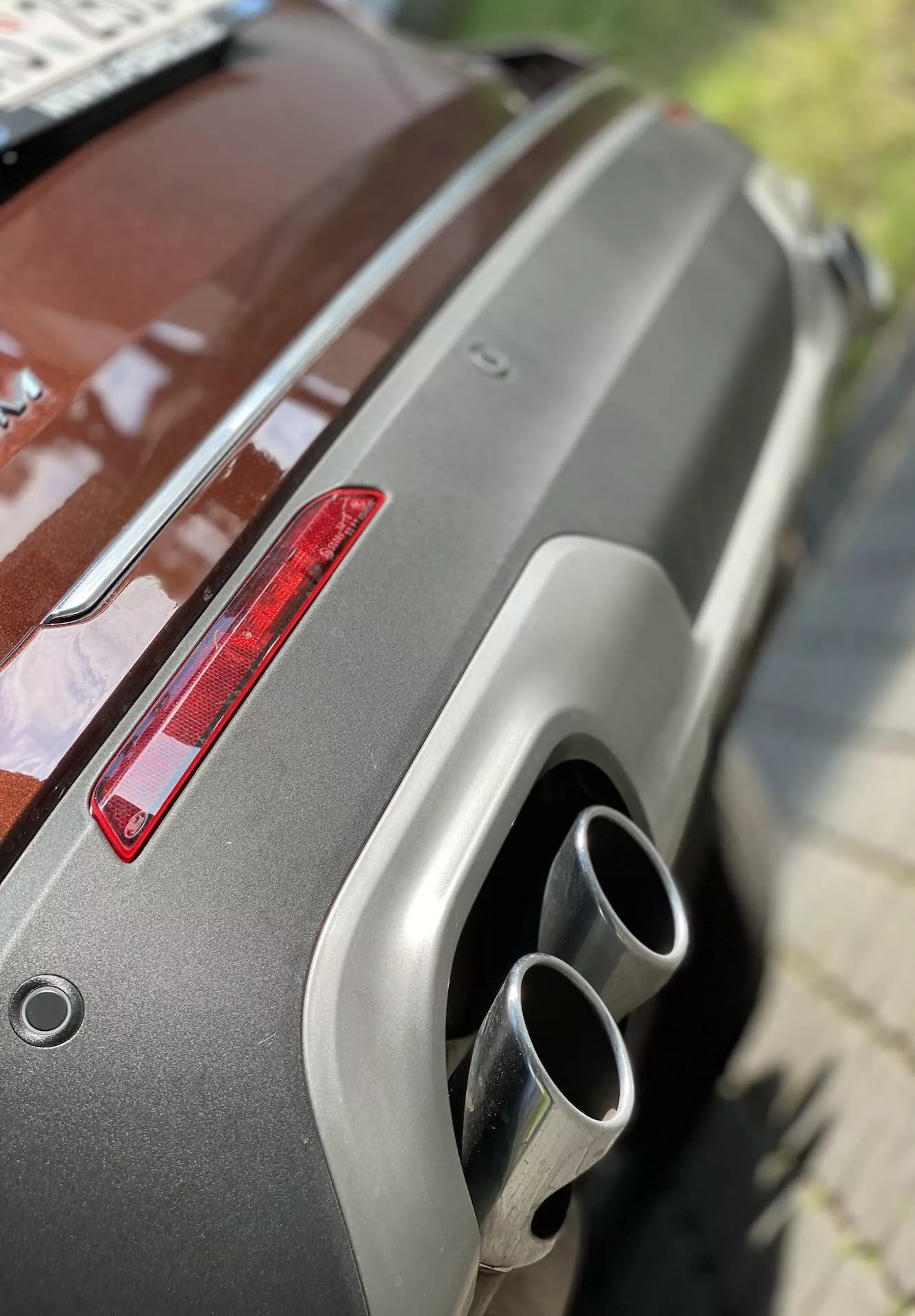 Close-up of the rear section of a 2019 Ford Explorer, showcasing the metallic paint, rear spoiler, red taillight, and dual chrome exhaust tips. The oblique angle from an elevated position highlights the well-maintained finish and modern design features.