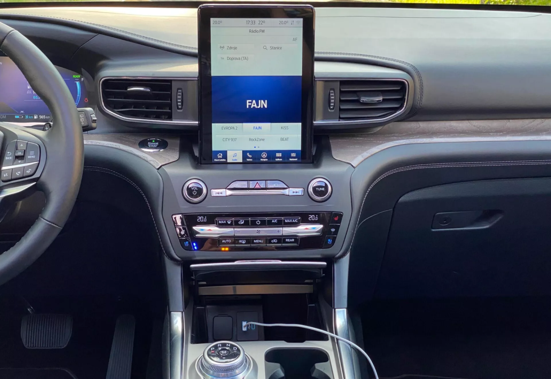 Interior of a 2019 Ford Explorer, showcasing the modern, central dashboard from a front or rear seat perspective. The dashboard features an upright infotainment touchscreen display with climate controls below, including dual climate control settings, a CD slot, and media input options. The central console includes a metallic-accented gear shift lever, control buttons, a rotary dial, and cup holders. The materials suggest a mix of wood grain, metallic finishes, and black plastic, highlighting the vehicle's technology and quality interior design.