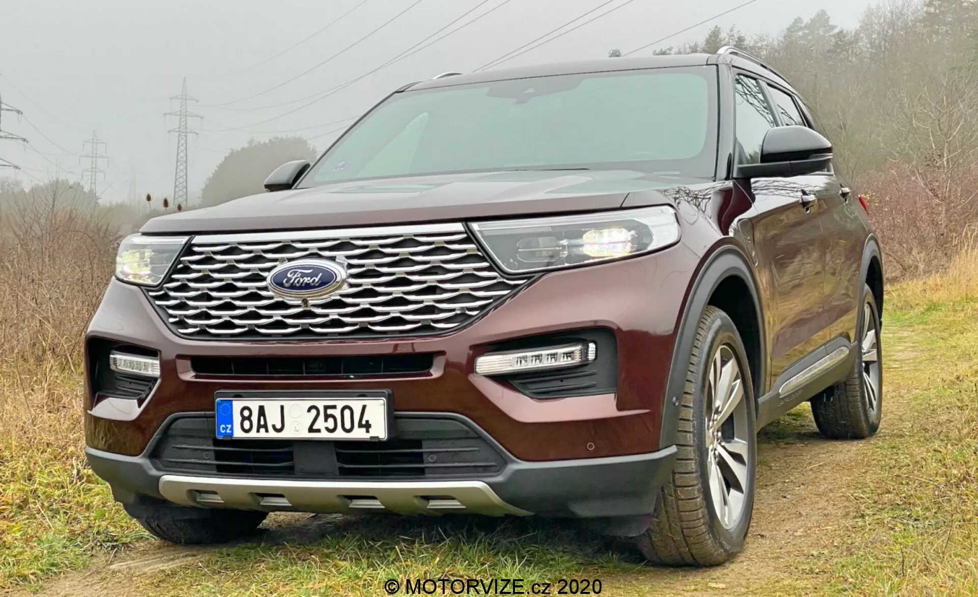 2019 Ford Explorer car photographed from a low front three-quarter angle showcasing the grille with Ford logo, headlights, fog lights, hood, side windows, and a portion of the rear. The vehicle's intricate grille design, sleek LED headlights, two-tone bumper, and keyless entry system emphasizes its modern and technologically advanced features. Positioned slightly off-road with right wheels on grass and left wheels on dirt, highlighting light off-road capability. Multi-spoke alloy wheels are visible, indicating all-season tires.