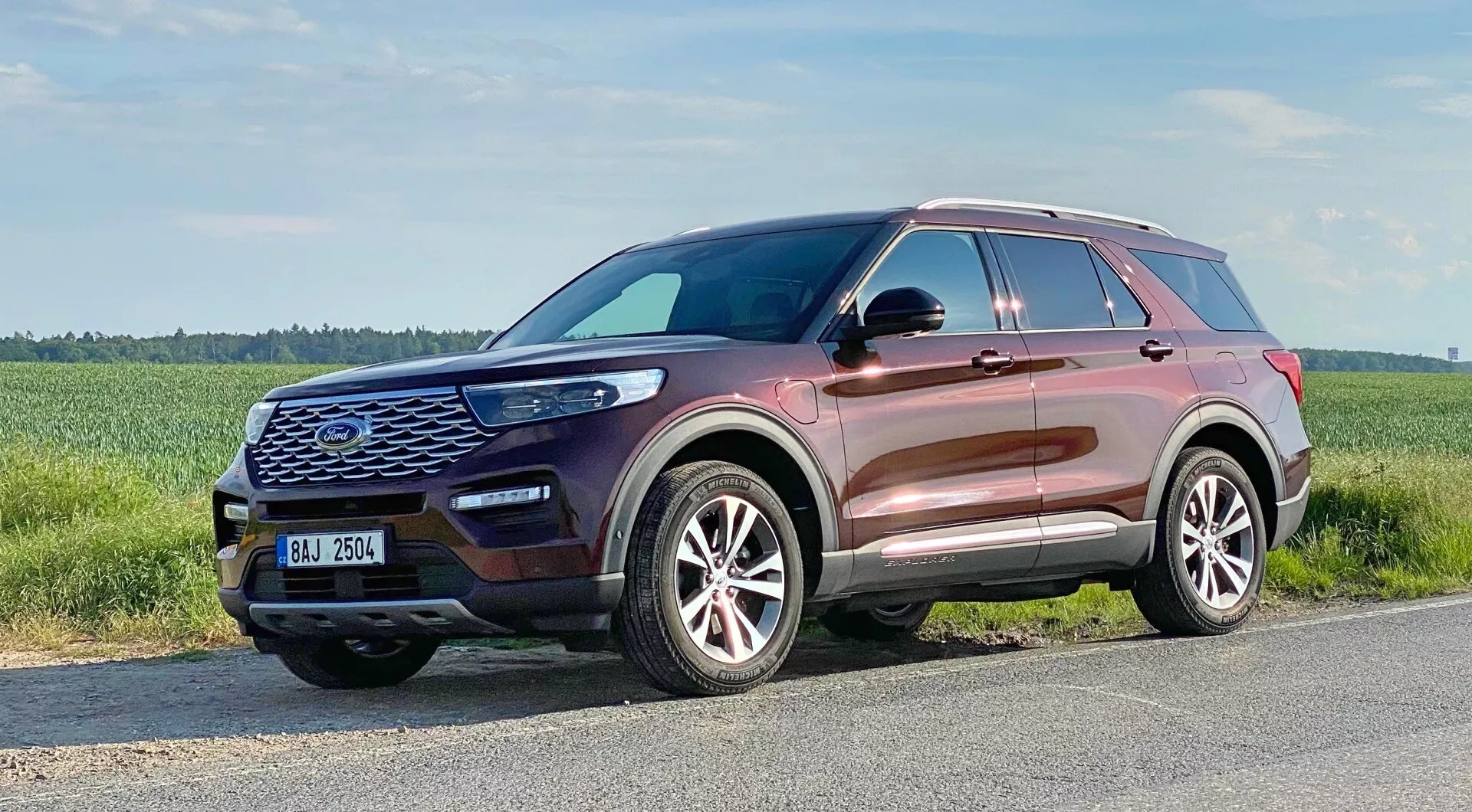 2019 Ford Explorer - A modern SUV captured from a three-quarter frontal view, highlighting its front grille with hexagonal pattern and large emblem, contoured hood, sleek LED headlights, fog lights, air intake vents, multi-spoke alloy wheels, slightly ascending window line, roof rails, integrated turn signal side mirrors, and metallic body color reflecting high-quality finish.