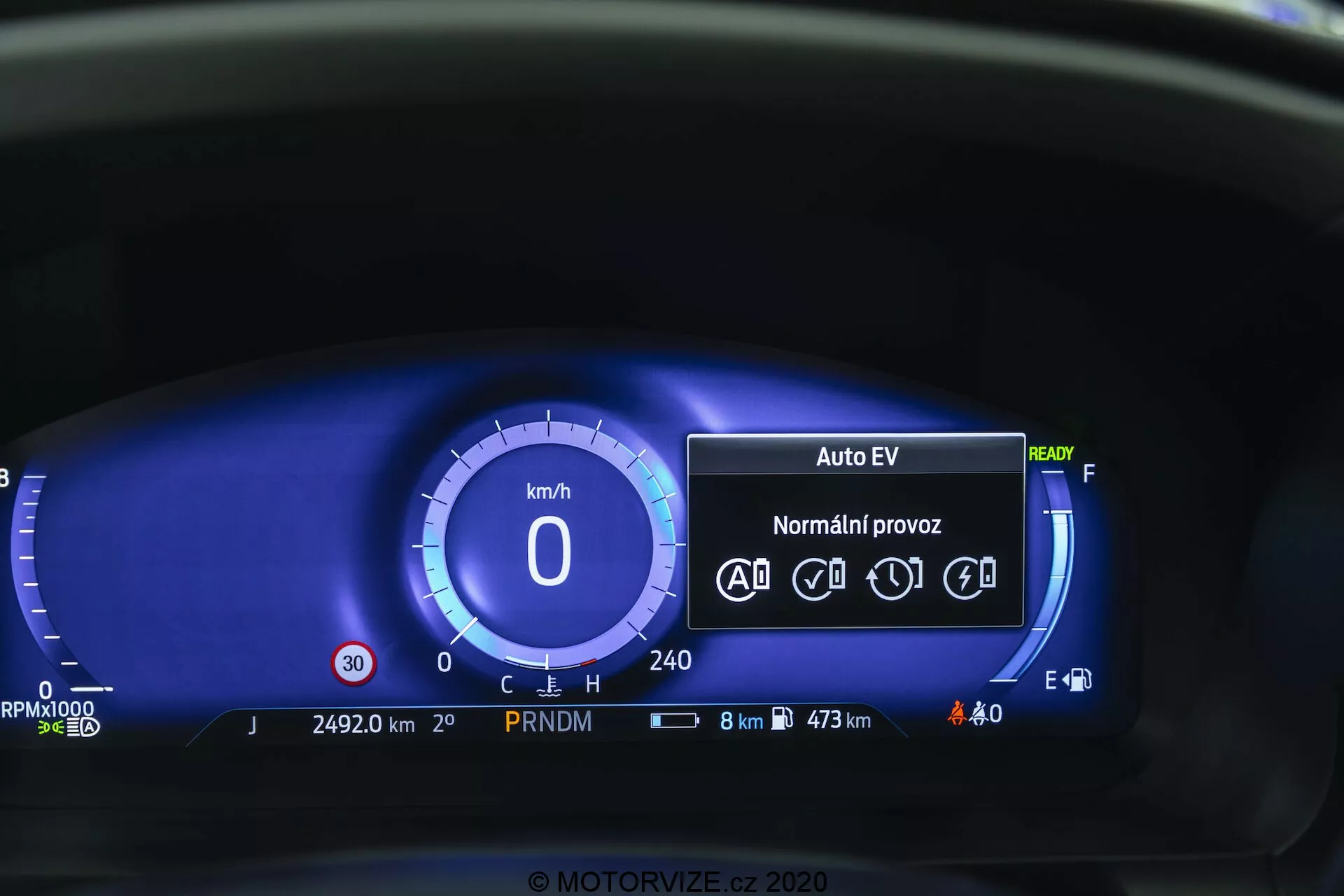 Close-up view of the Ford Explorer 2019 digital instrument cluster from the driver's perspective. Digital speedometer shows 0 km/h and instrument panel includes 'Auto EV' mode, indicating an electric or hybrid drive system, 'Ready' status, icons for automatic driving functions, odometer at 24,920 km, PRNDM gear indicator, status icons for battery and exterior lighting, fuel economy readout of 8 km remaining with max range of 473 km, digital fuel gauge, and no warning lights. The blue color theme offers a modern aesthetic.