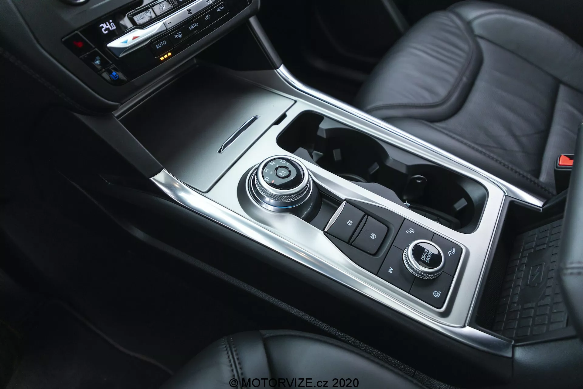 Interior shot of the 2019 Ford Explorer focusing on the center console from a top-down angle, showcasing the gear shift knob, infotainment and vehicle control system, cup holders, storage space with USB ports, climate control dials, and leather-upholstered center armrest, with a combination of metal, leather, and plastic components, emphasizing modern aesthetics and functionality.