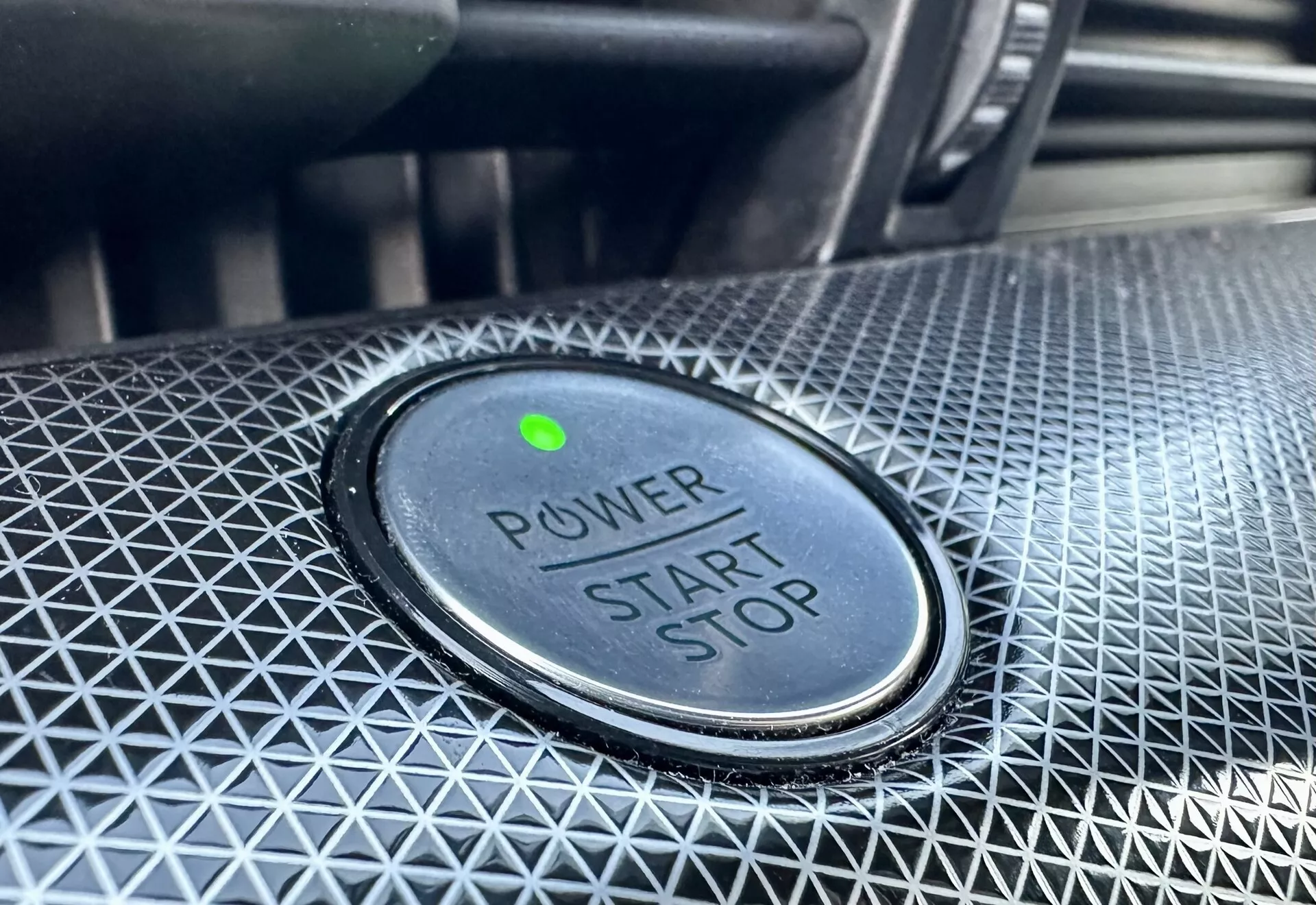 Close-up view of the power start/stop button in a 2020 Ford Mustang-Mach-E, featuring 'POWER START STOP' text, green indicator light, and textured surrounding design