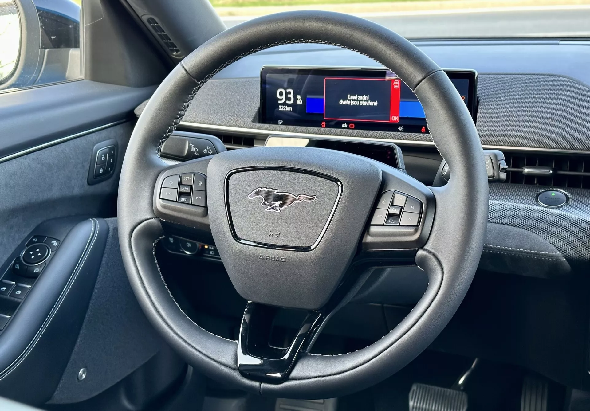 2020 Ford Mustang Mach-E interior highlighting the modern three-spoke steering wheel with multifunction buttons and digital instrument cluster from a driver's perspective, showcasing controls, emblem, and navigation hints.