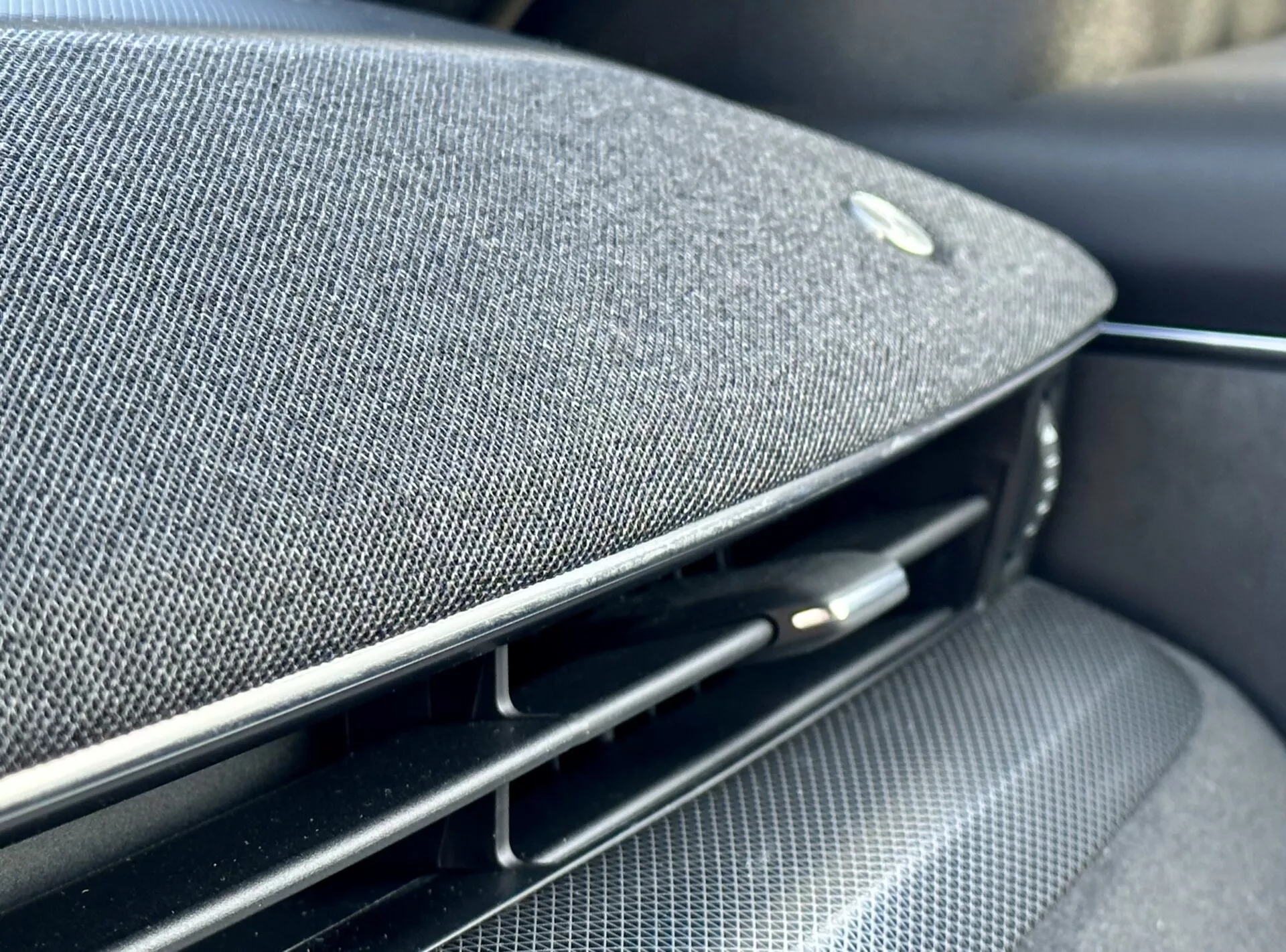 Close-up view inside the 2020 Ford Mustang Mach-E showcasing a part of the dashboard or door panel with an integrated premium fabric speaker grill, an emblem suggestive of a high-end audio partnership, alongside a glossy black air vent