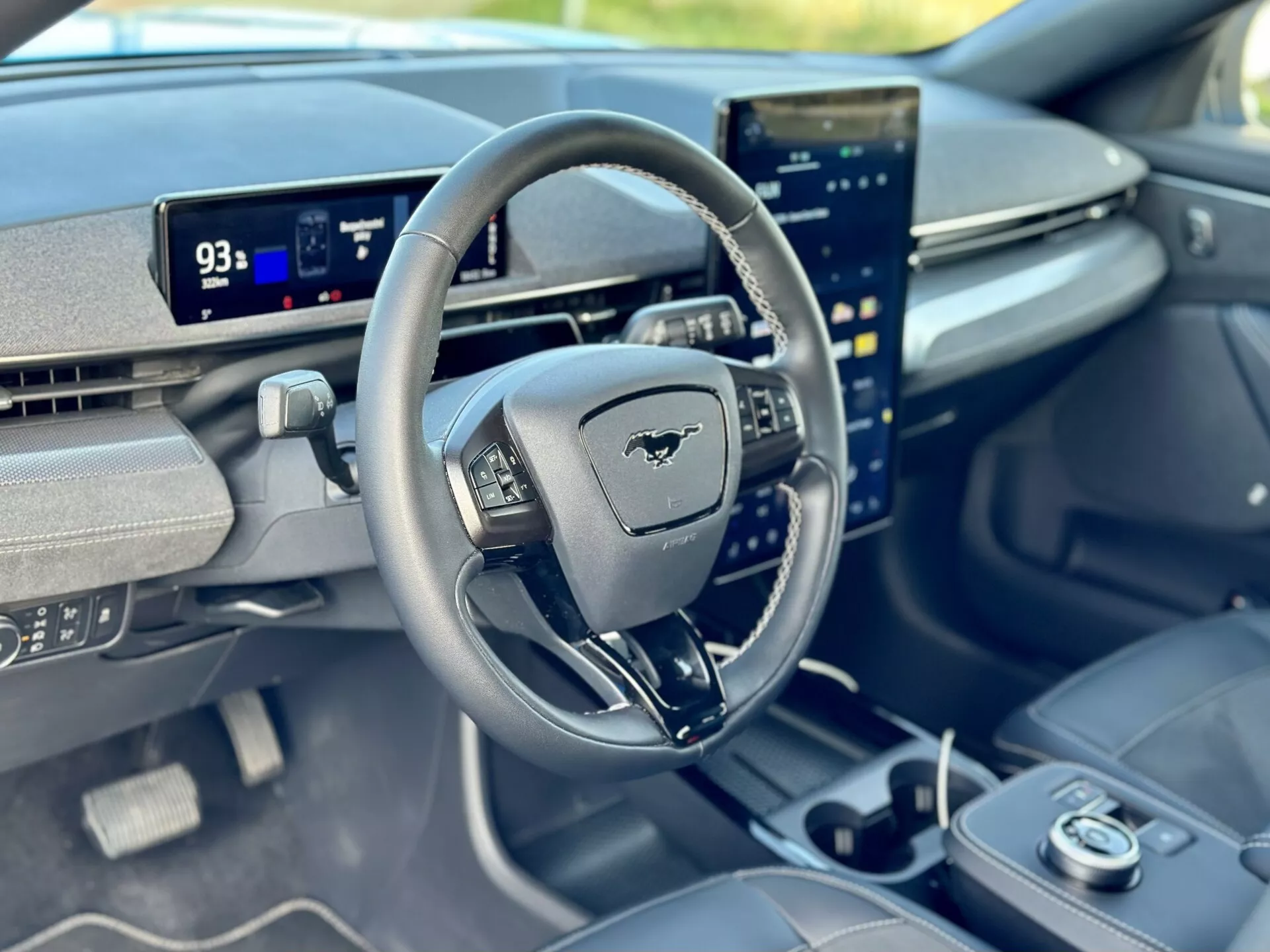 Interior view of a 2020 Ford Mustang Mach-E focusing on the driver's cockpit from the front passenger perspective, featuring a steering wheel with Mustang emblem, digital dashboard in Park mode showing 93 miles range, and a vertically oriented central touchscreen integrated with advanced infotainment capabilities.
