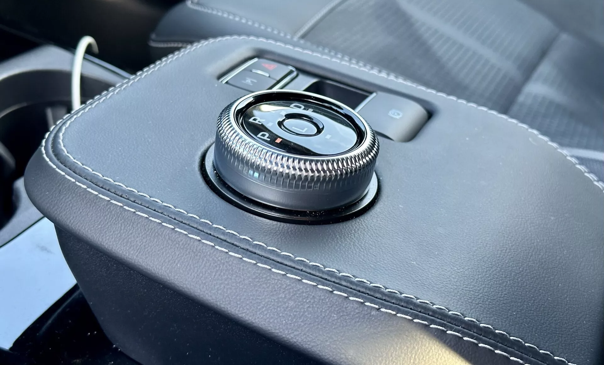 Close-up view of the Ford Mustang Mach-E 2020 interior featuring a central console rotary dial control on a leather-wrapped surface with white stitching, providing an ergonomic infotainment interface