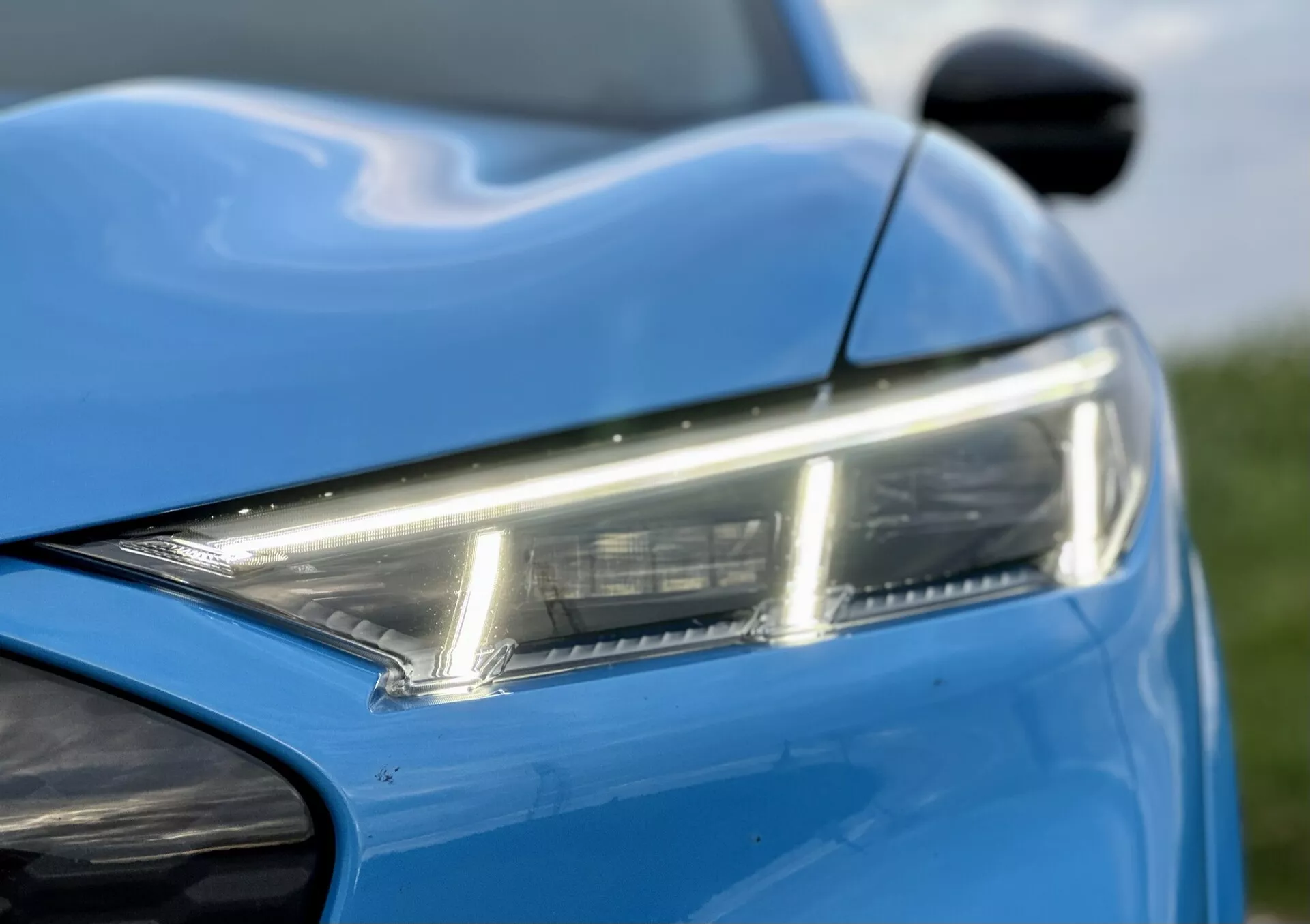 Close-up view of a 2020 Ford Mustang-Mach-E highlighting the sleek LED headlight, vibrant blue paint, and dynamic body lines, with a glimpse of the side mirror and front bumper, showcasing modern design and aesthetics.