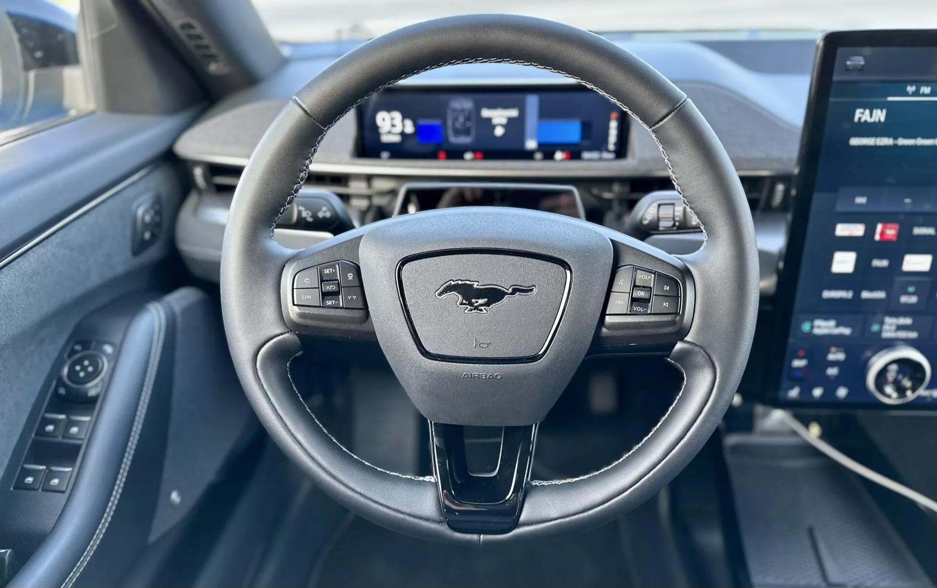 Interior view of a Ford Mustang-Mach-E 2020 from the driver's perspective, featuring a three-spoke steering wheel with controls, a digital instrument cluster, and a large infotainment touchscreen