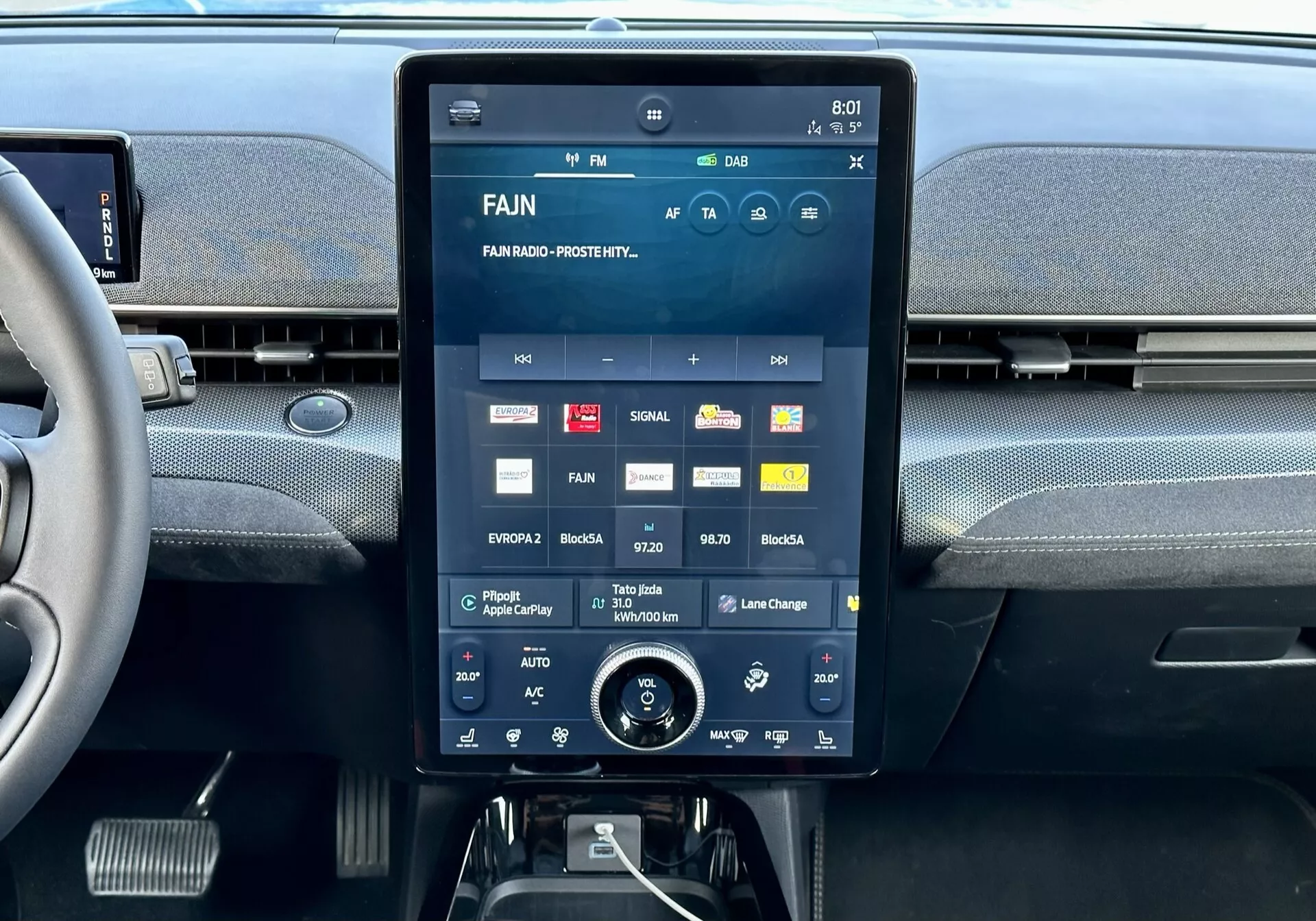 Ford Mustang Mach-E 2020's interior central console featuring a large touchscreen display showcasing multimedia interface with apps and settings, integrated air vents above, and additional climate control rotary dial below.