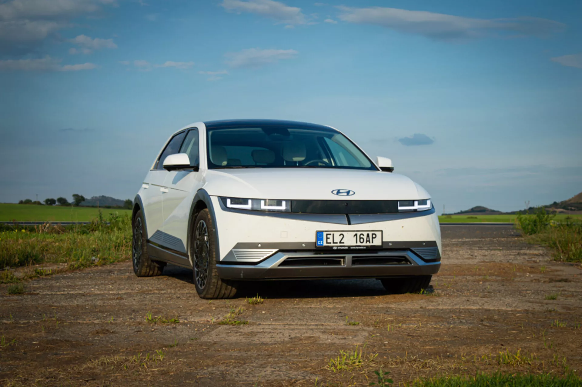 2021 Hyundai Ioniq 5 electric car showcasing modern design with sleek hood, distinctive LED daytime running lights, closed-off grille for aerodynamics, and sporty wheels, taken from a low front angle to emphasize the car's front-end styling and stance, parked outdoors under a blue sky