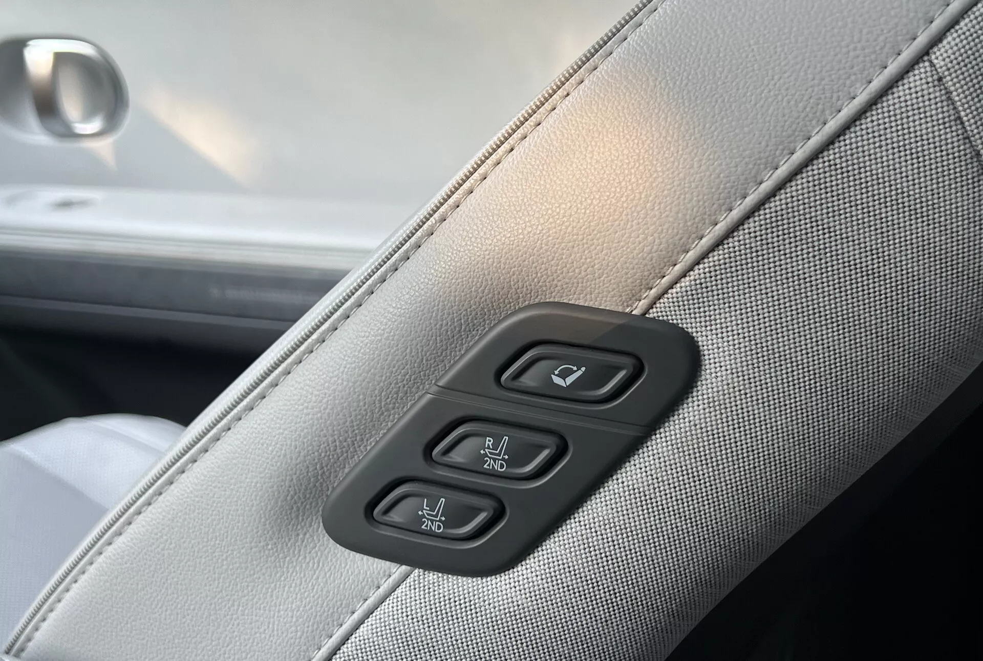2021 Hyundai Ioniq-5 interior detail showing light gray synthetic or leather upholstery with darker gray stitching and controls for power windows and door locks on a piano black background