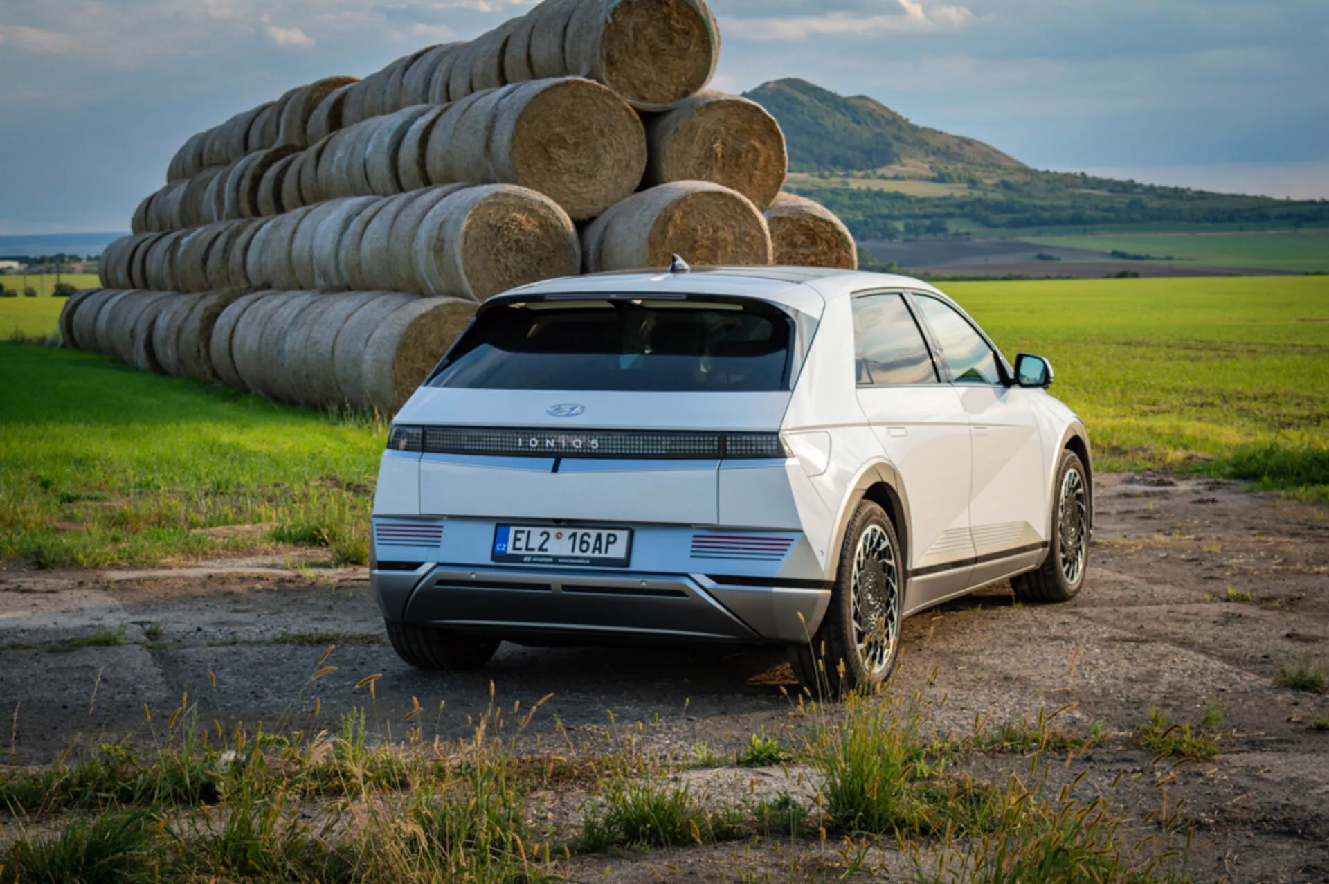 2021 Hyundai Ioniq 5 electric SUV in white, showcasing rear three-quarter view with LED taillights, stylish alloy wheels, and sensors against a backdrop of an open field and hay bales under clear daytime sky