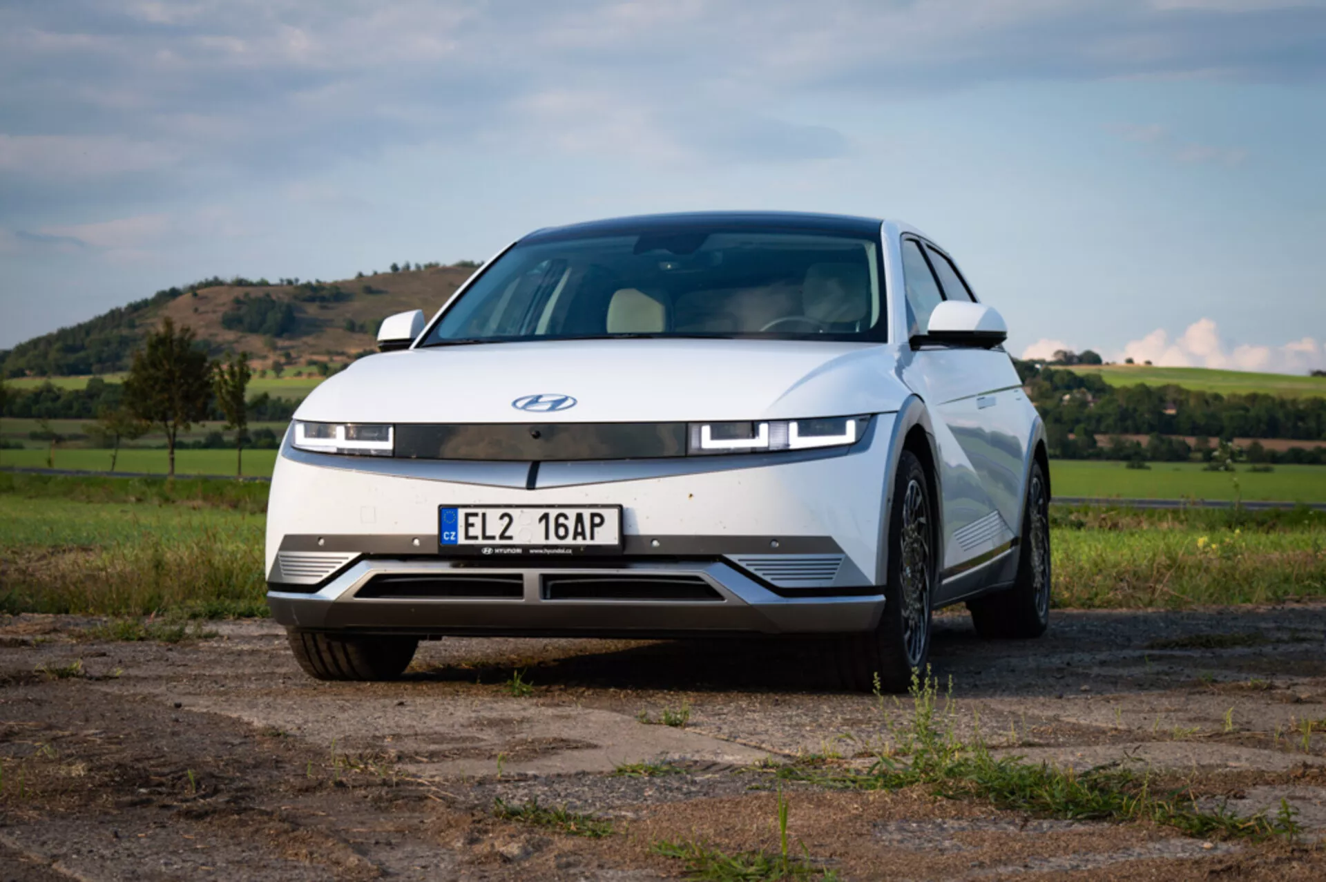 Low front angle view of a Hyundai Ioniq 5 2021 parked outdoors showcasing its full front facade and partial profiles with detailed design elements like LED headlights and lack of traditional grille, set against a natural backdrop with visible hills and open sky.
