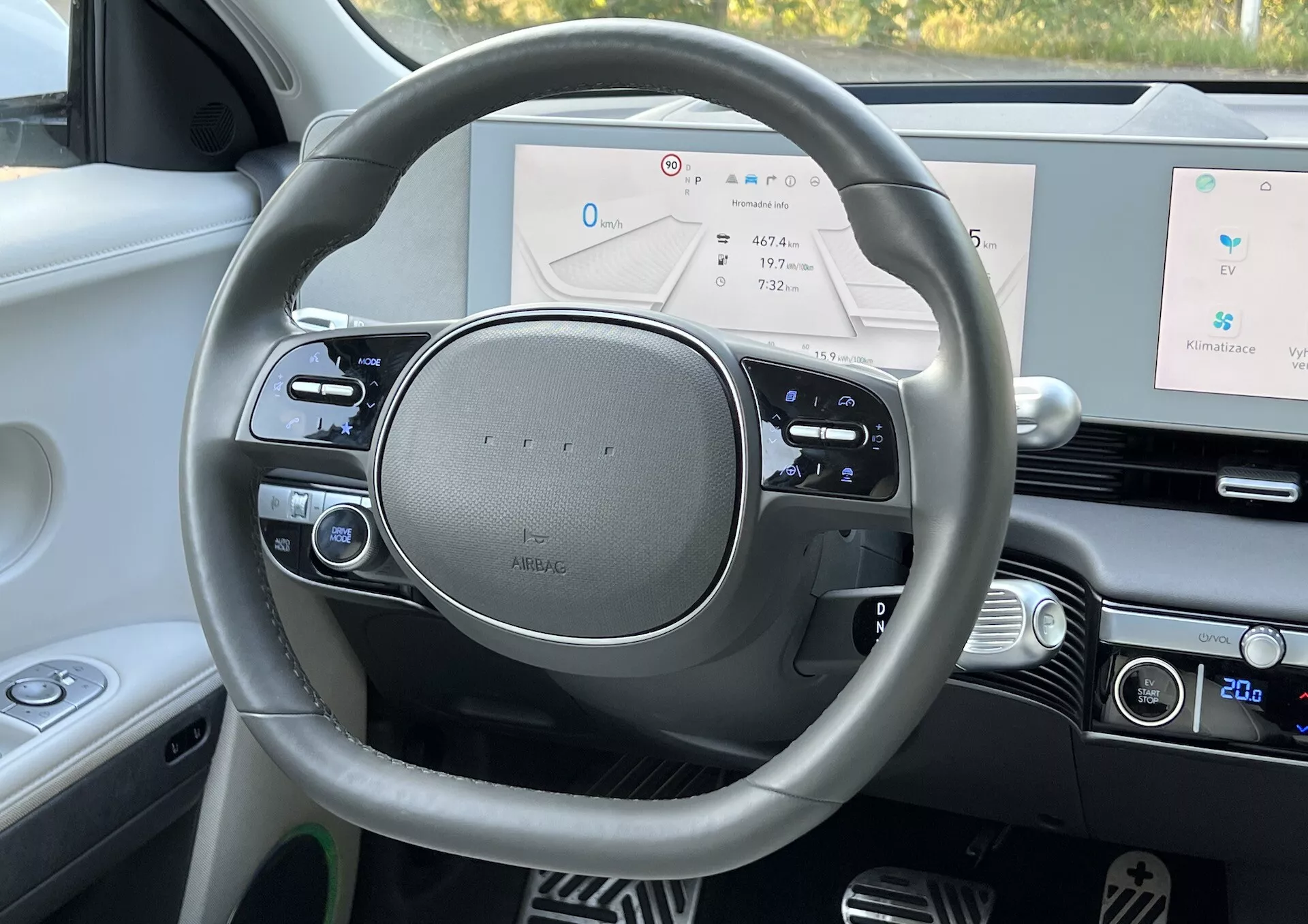 First-person perspective view of the Hyundai Ioniq 5 2021 interior focusing on the modern steering wheel with silver emblem, digital dashboard displaying speedometer, navigation, and system status, alongside high-quality interior design details