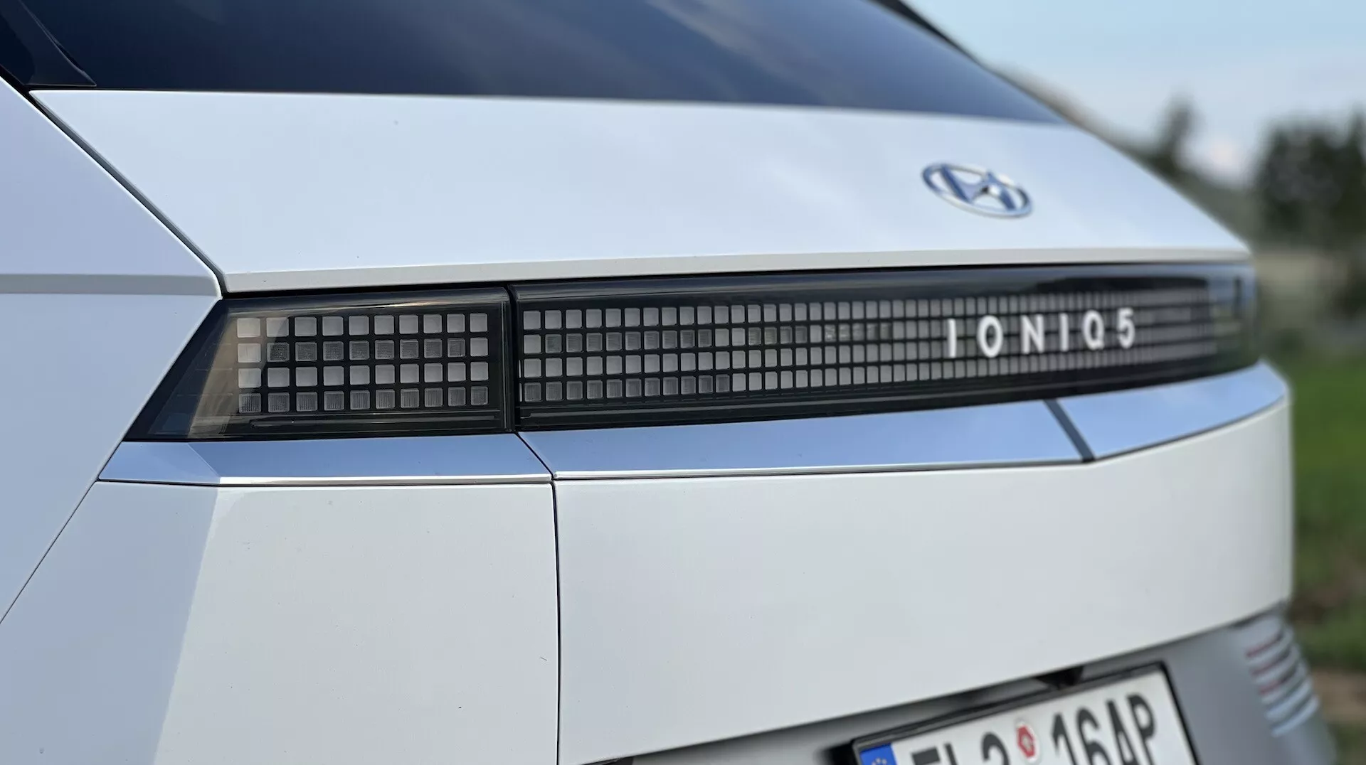 Close-up view of a 2021 Hyundai Ioniq 5's rear end, highlighting the brand emblem, model name, and advanced LED light bar, against a blurred outdoor backdrop.