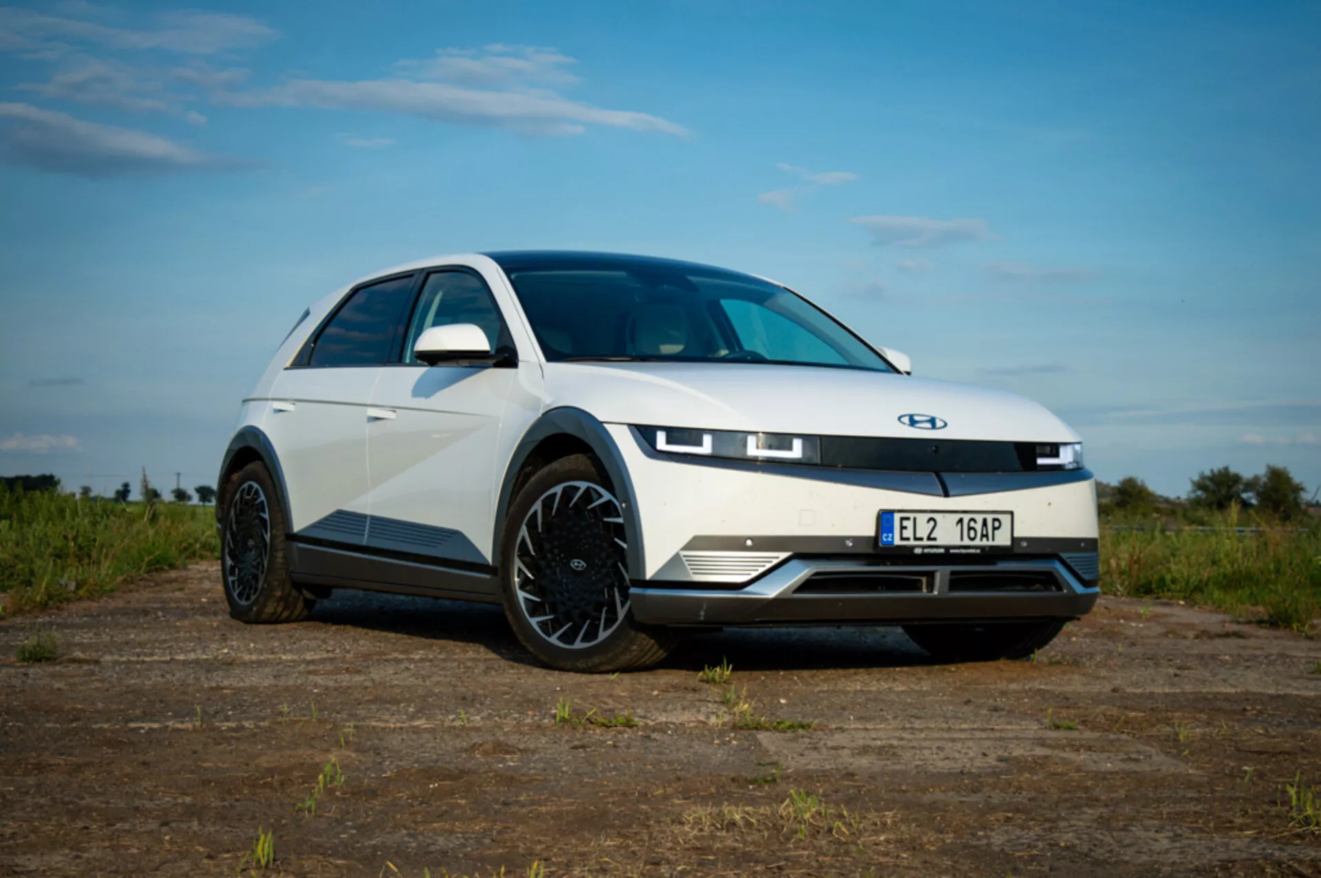 Low-angle view of a 2021 Hyundai Ioniq 5 highlighting LED headlights, aerodynamic alloy wheels, and sleek bodywork on a dirt background with a partly cloudy sky