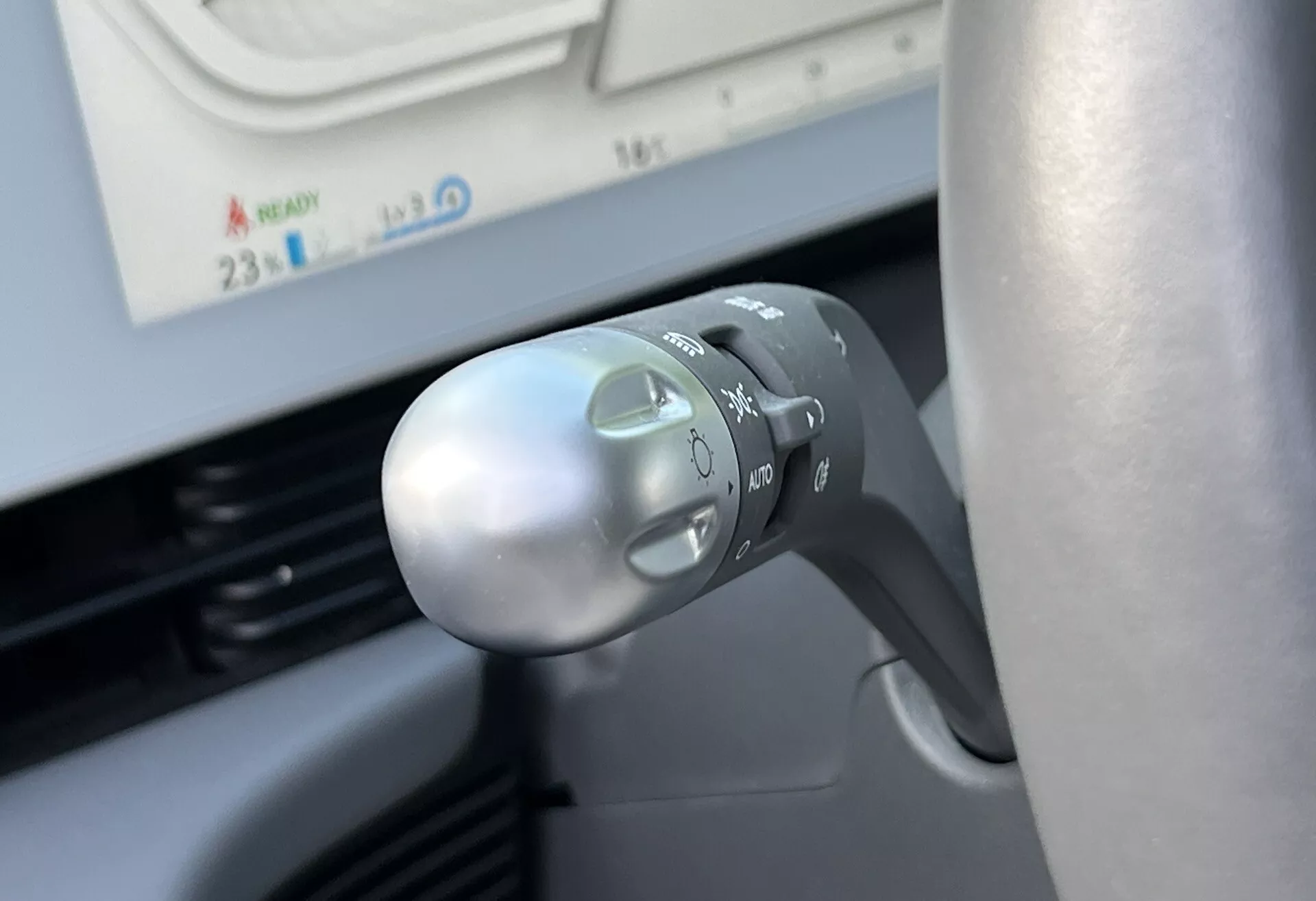 Close-up view of Hyundai Ioniq-5 2021 turn signal and light control stalk on steering column, showcasing symbols for headlights, auto mode, turn signals, and ergonomic design from a driver's perspective