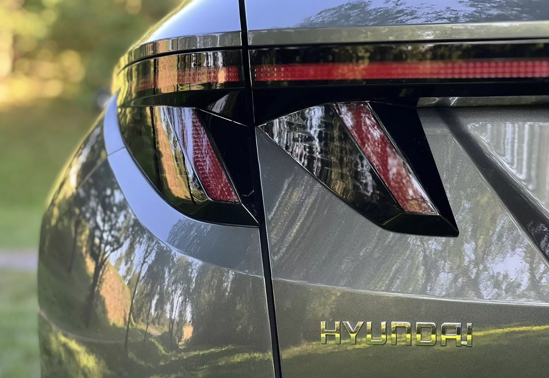 Close-up view of the 2020 Hyundai Tucson's rear section, showcasing angular LED tail lights, HYUNDAI branding, integrated rear spoiler with brake light, and glossy metallic finish