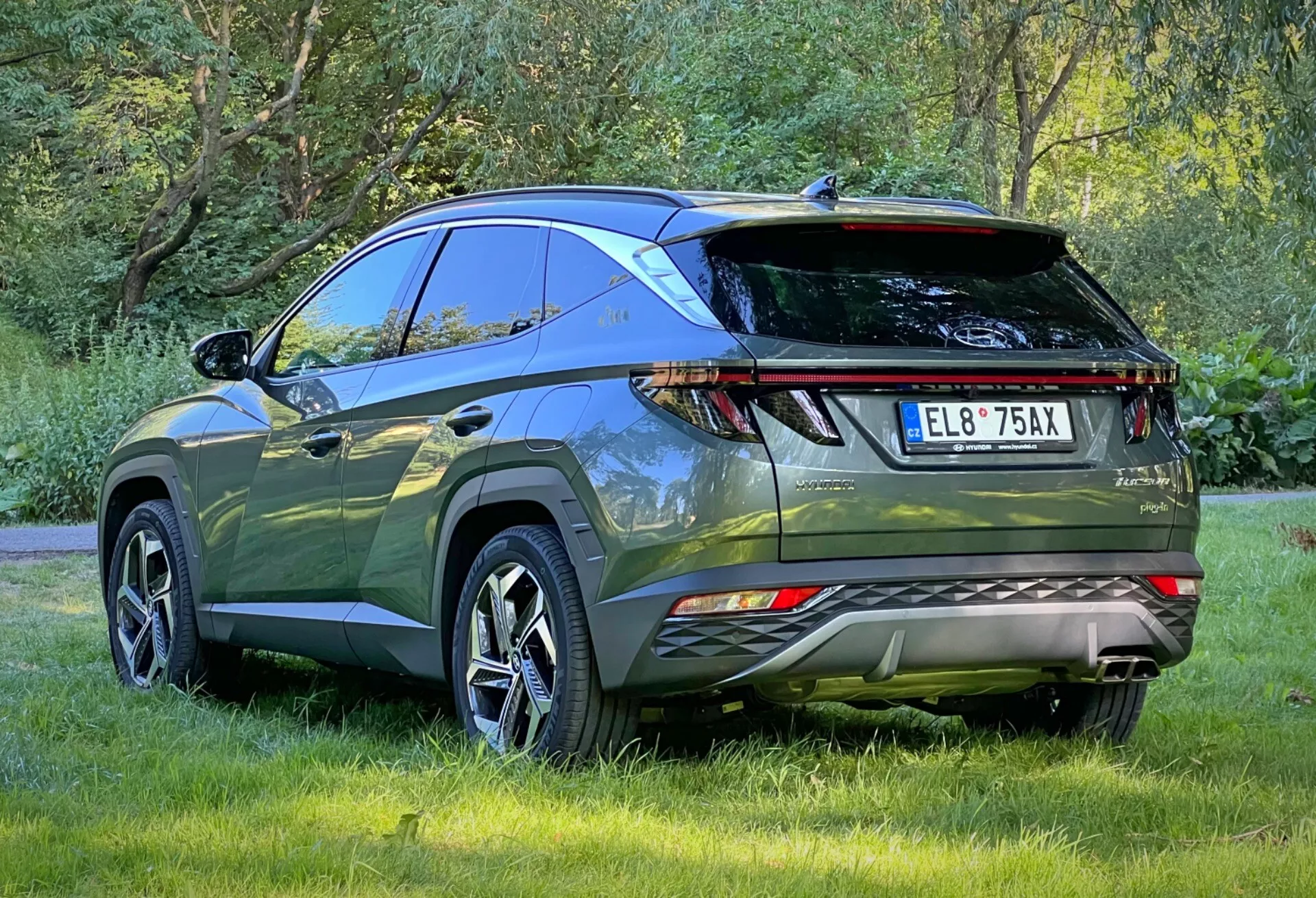 2020 Hyundai Tucson rear three-quarter view highlighting LED tail lights, parking sensors, dual exhaust, sporty rear spoiler, and roof rails, parked outdoors on grass showcasing a modern crossover SUV's aerodynamic design and advanced features for outdoor adventure and practical use.