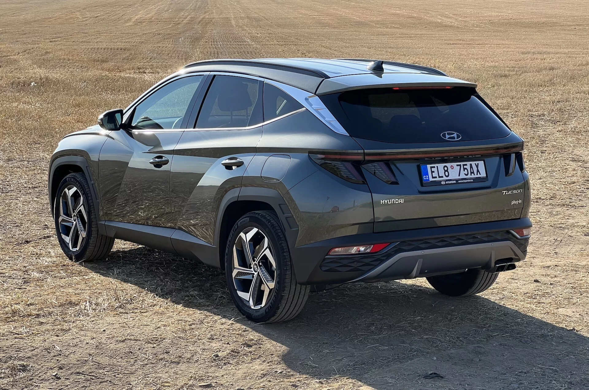 2020 Hyundai Tucson modern SUV in oblique view showcasing rear and side profiles with hybrid technology badge on dry grassy field, highlighting LED taillights, contrasting bumper insert, and sporty multi-spoke wheels
