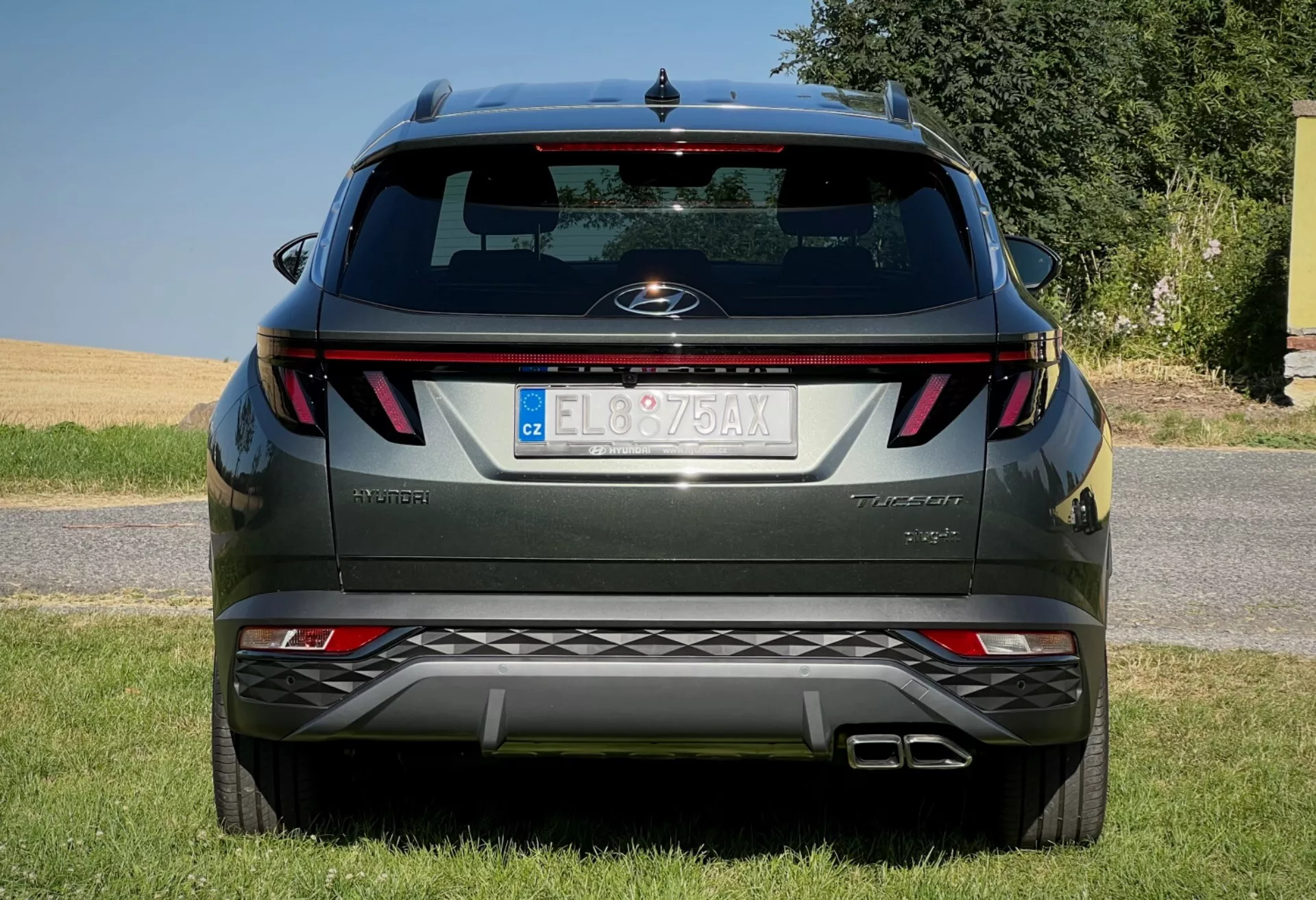 2020 Hyundai Tucson rear view showcasing horizontal taillights, central badge, trim level name, integrated parking sensors on the bumper, and a dual exhaust system, parked on a grass-lined surface against a clear sky