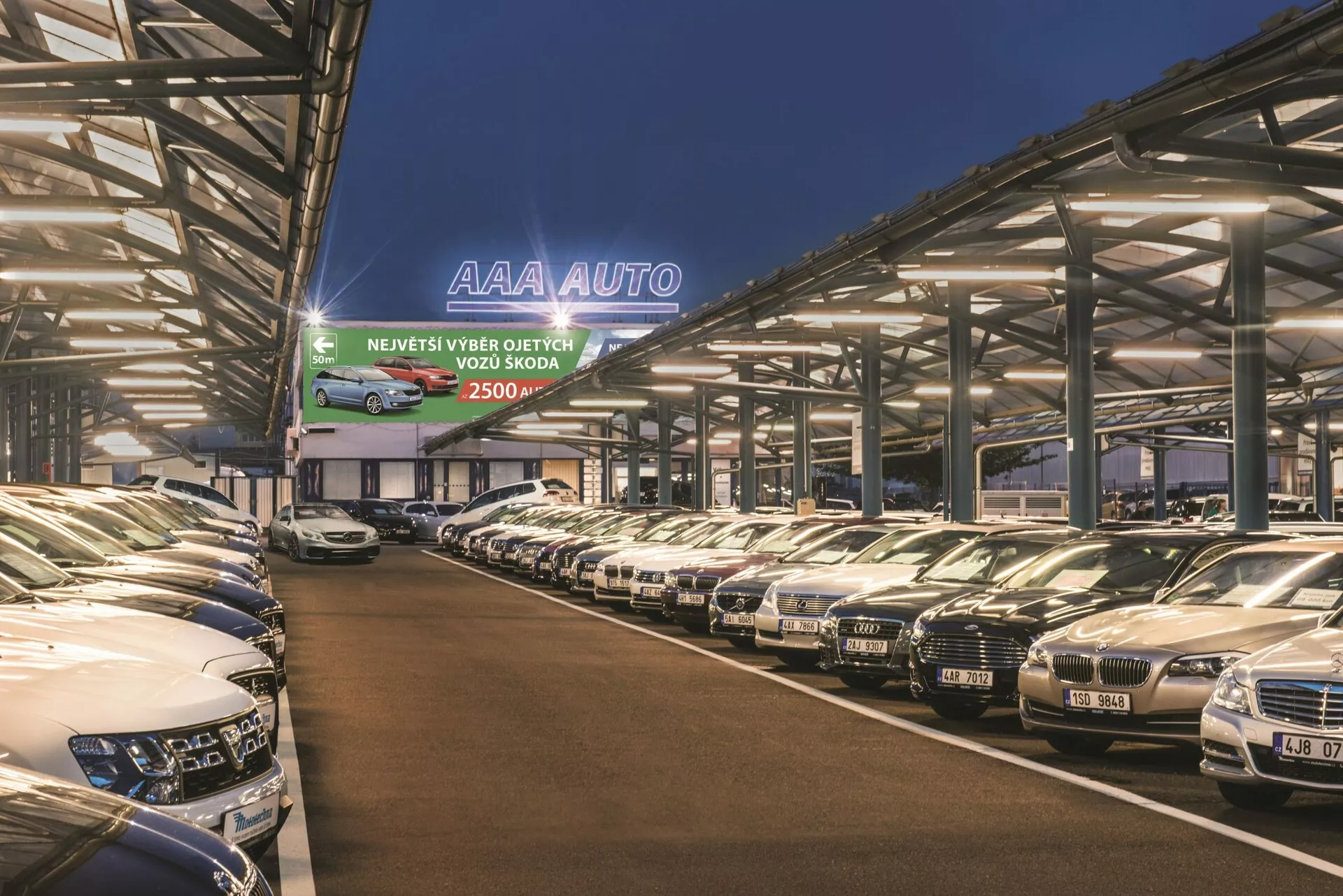 2018 Hyundai Tucson arrayed in a large, covered dealership lot under dusk sky, showcasing diverse models and front-end designs with 'AAA AUTO' signage illuminated in the background