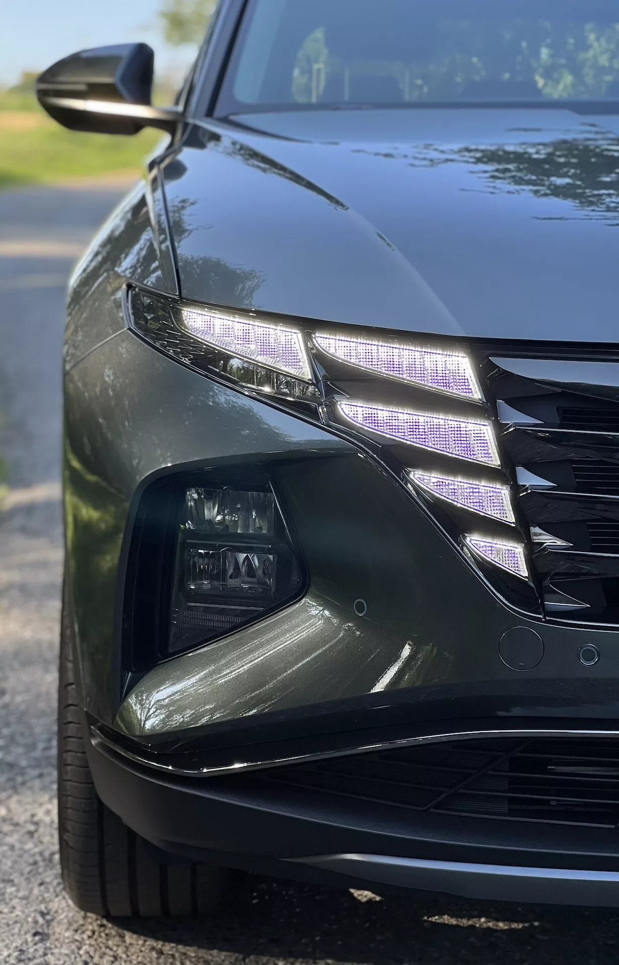 Close-up angled view of a 2020 Hyundai Tucson showing intricate LED headlight design and part of the grille with a glossy finish under low-light conditions, illustrating luxury car features and modern automotive lighting technology.