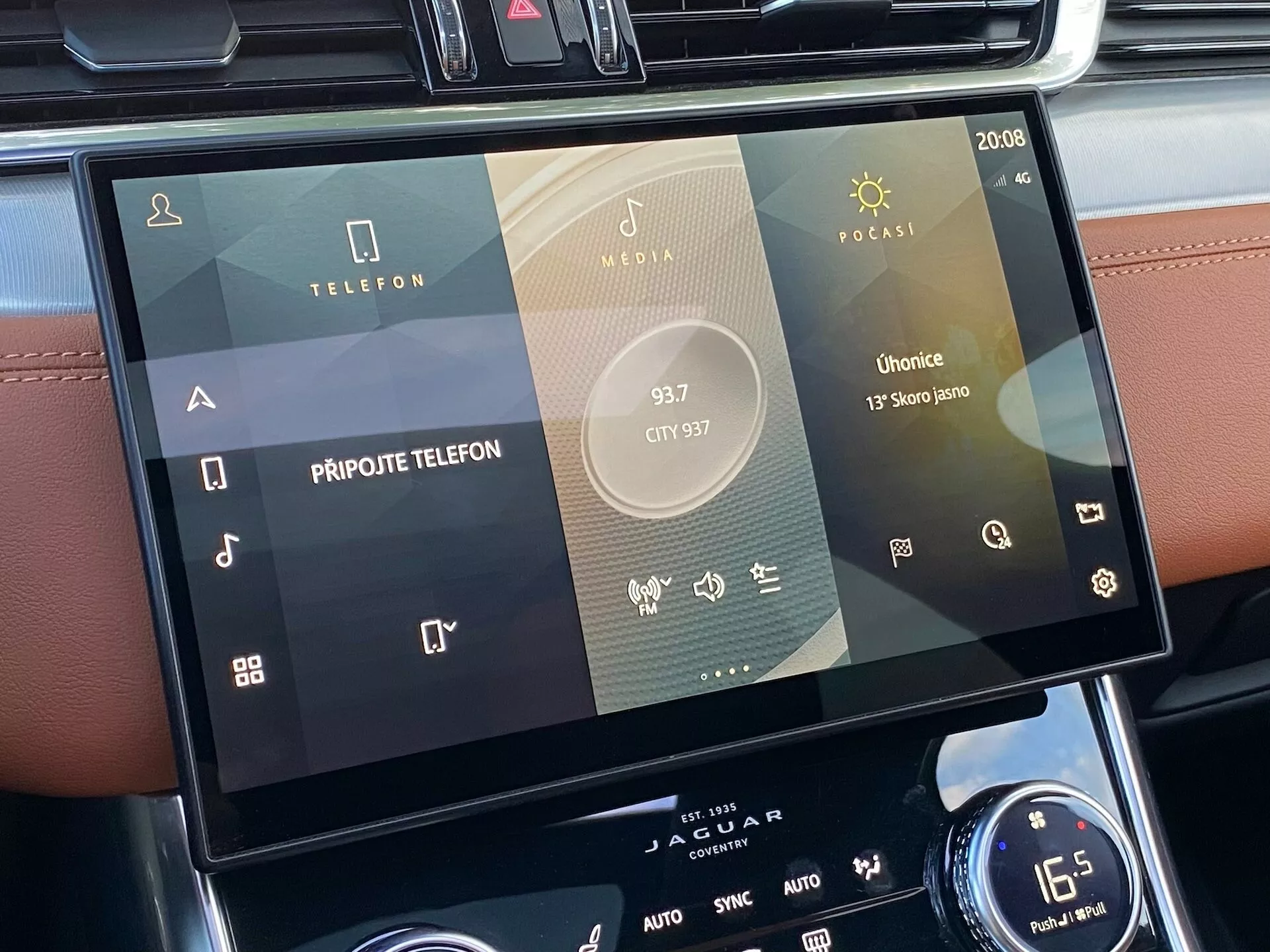 2021 Jaguar XF in-car touchscreen infotainment system positioned in the central console, viewed from the perspective of a passenger or driver. The focus is on the screen, displaying multiple icons for telephone connectivity, media playback, and vehicle-specific applications including Radio, Media, and Podcasts, with signs of smartphone integration. Modern touch-based interface with sleek design, showing system settings such as time (20:08) and AUTO for climate control. Below, rotary dial and dual-zone climate controls with a temperature setting of 16.5 degrees Celsius are visible.
