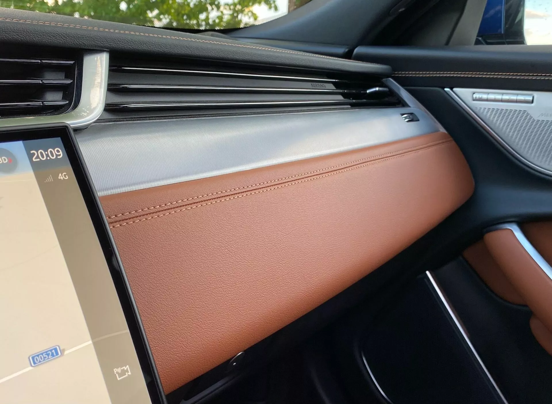 Interior view of 2021 Jaguar XF from the front passenger seat, showcasing the right side of the dashboard, infotainment screen, and passenger door. Features include a chrome-outlined air vent, integrated infotainment touchscreen displaying time and 4G signal, wood veneer trim, stitched leatherette, and glossy black finishes, reflecting luxury design and advanced technology.