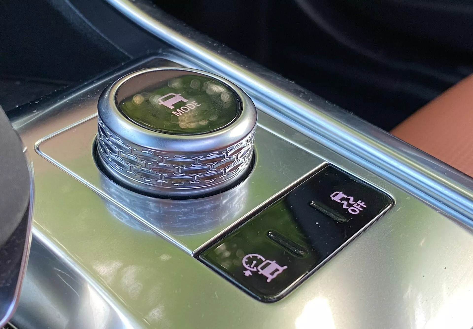 This image captures a section of the 2021 Jaguar XF's interior, focusing on the gear shift area from a top-down perspective. The central feature is a circular gear shift knob with a reflective metallic finish and an illuminated display indicating 'P' mode. Surrounding the knob is a patterned detail, and below it lies a glossy panel with touch-sensitive controls, including an electronic parking brake control and a possible parking assist system control. The luxurious materials such as polished black surfaces and possibly wood grain or brushed metal accents exemplify the premium design aesthetics of this car's interior.