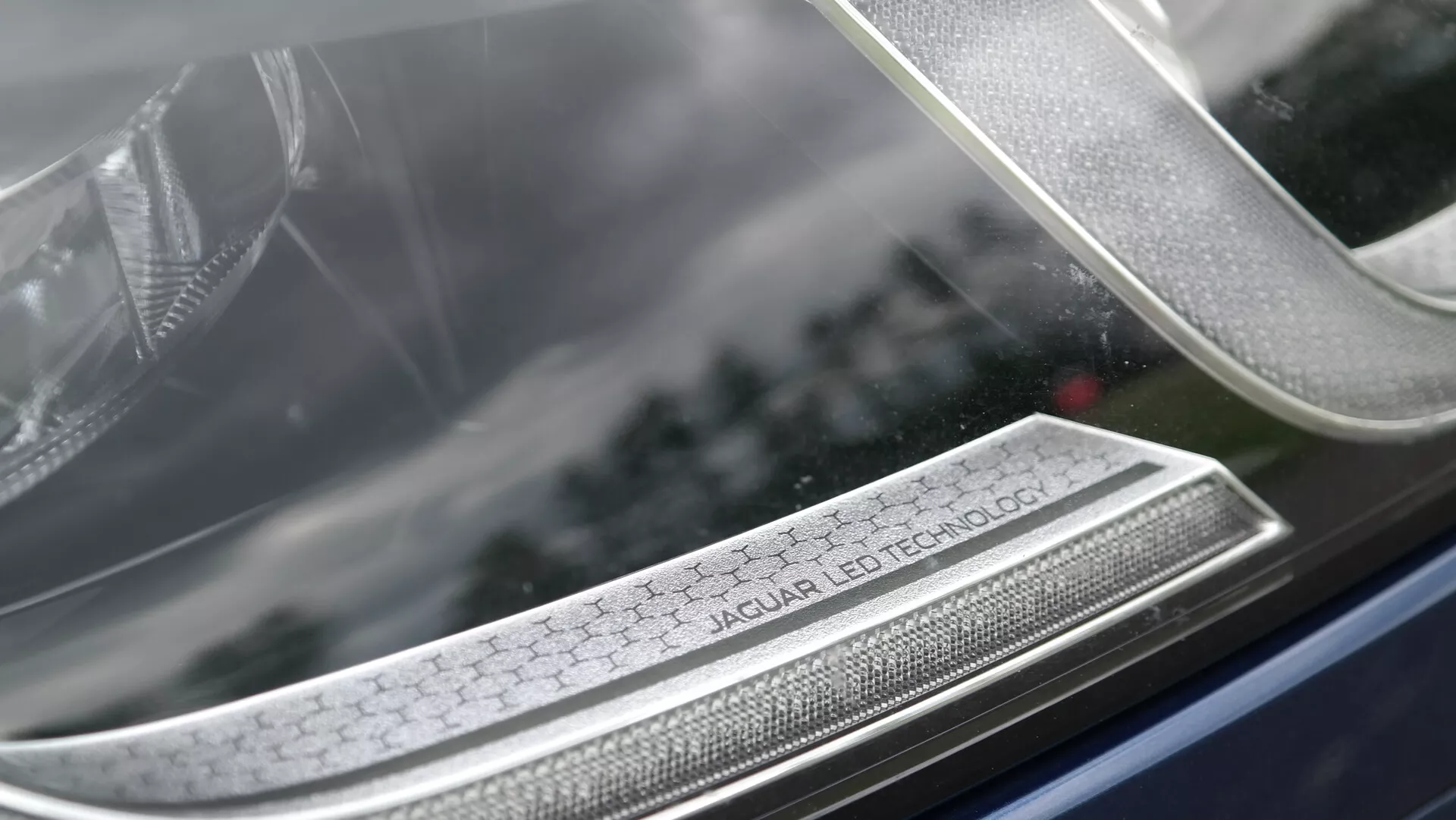 Close-up of Jaguar XF 2021 headlight featuring 'Jaguar LED Technology' inscription, showcasing advanced LED lighting, luxury design, and detailed craftsmanship with a blurred background emphasizing the headlamp's intricate array.
