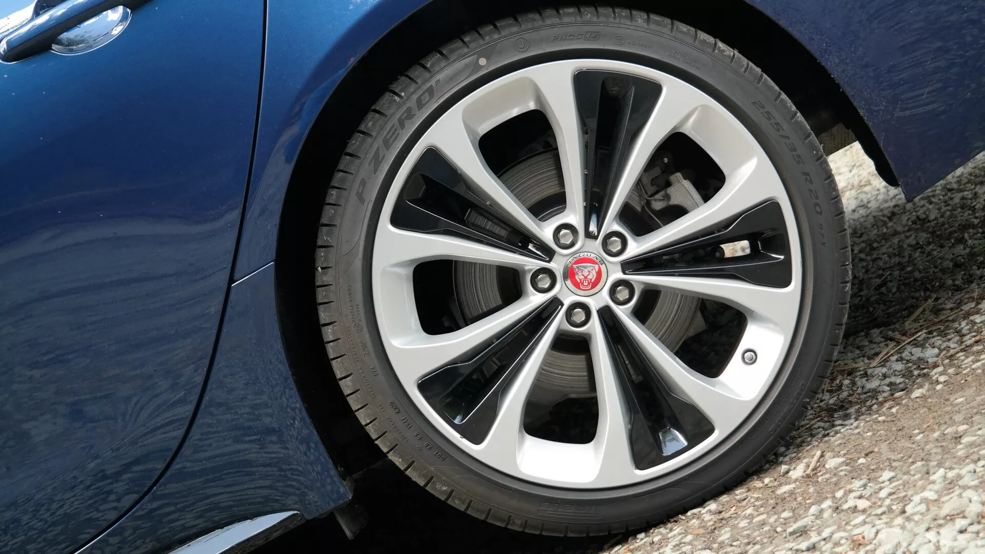 Close-up view of the Jaguar XF 2021 driver’s side front wheel from a low angle showcasing a stylish multi-spoke alloy design with metallic silver and darker shaded finishes, detailed tire tread pattern, and reflective metallic paint finish on the lower part of the car's side panel.