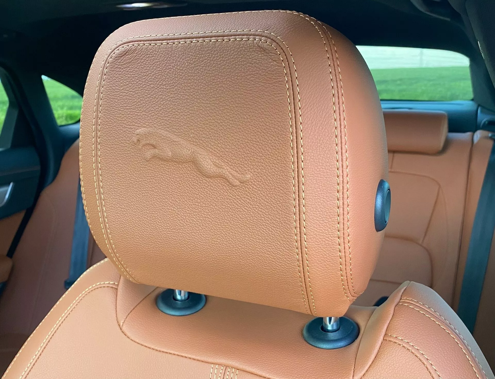 Close-up view of the Jaguar XF 2021 backrest headrest, showing tan leather with stitched horse emblem, suggesting luxury features. Blue circular elements at the base indicate possible adjustable mechanisms.