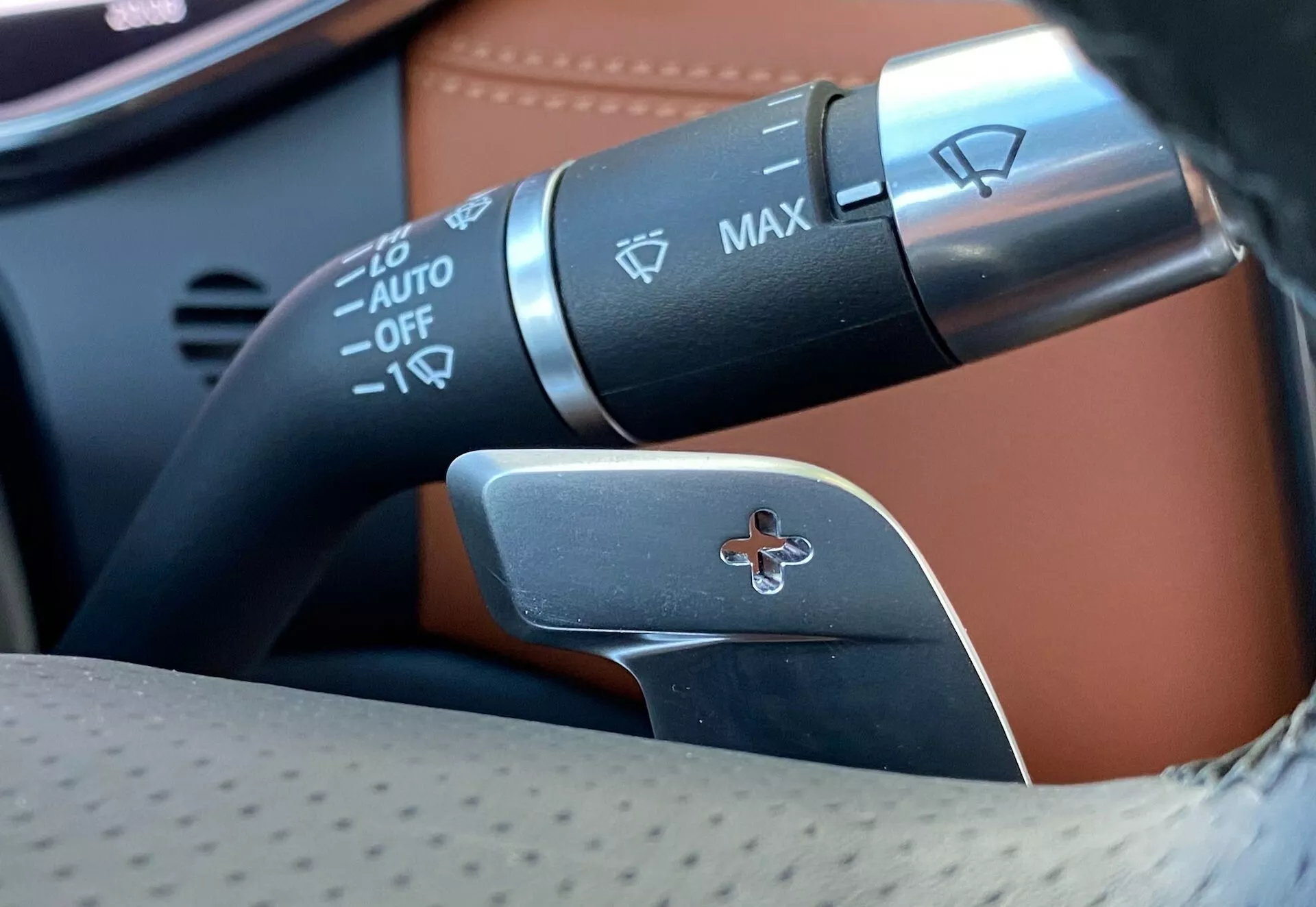 Close-up view of Jaguar XF 2021 steering wheel column showcasing control stalks; includes turn signal and headlight control stalk with automatic headlight, fog lights control, and paddle shifter for manual gear selection.