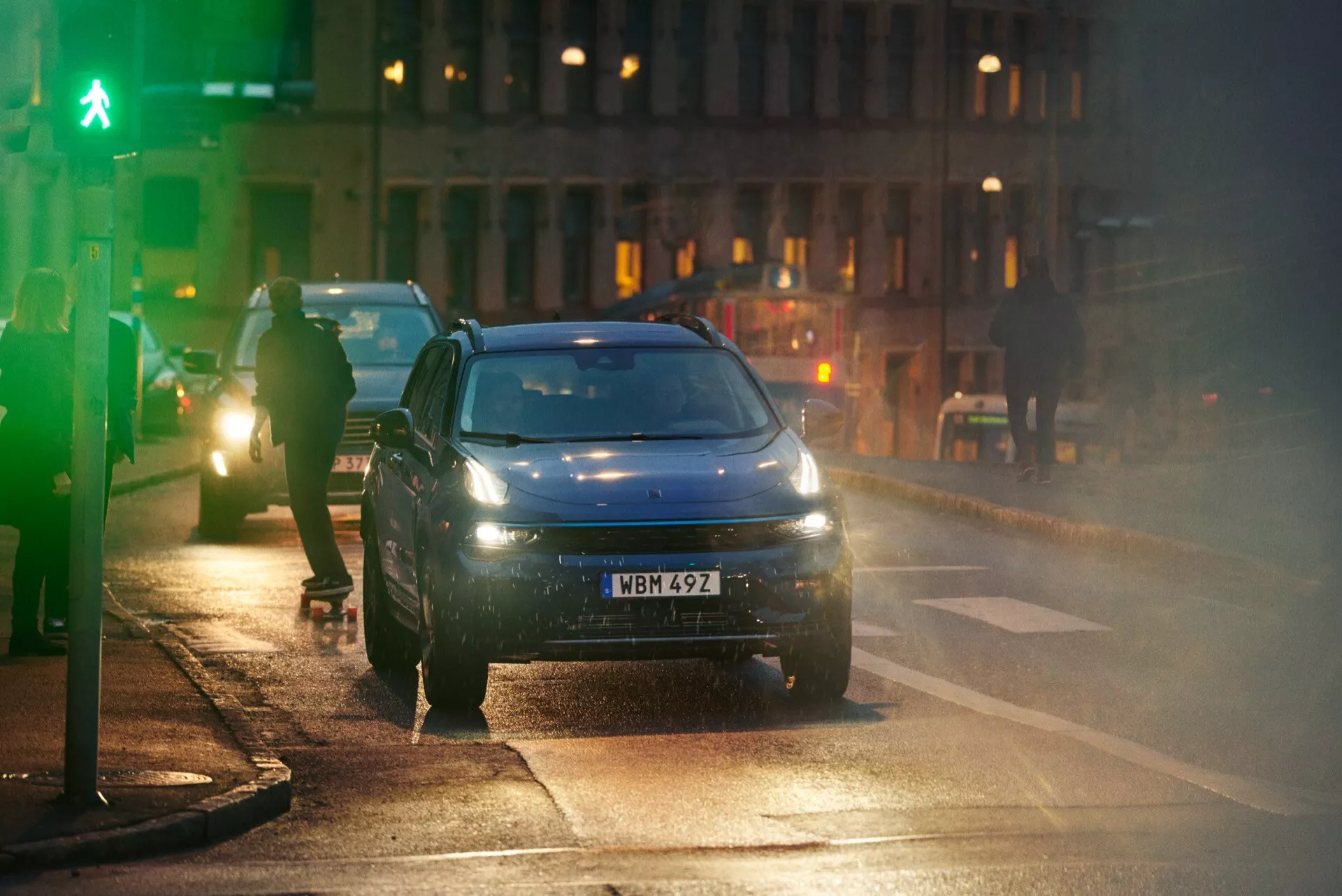 2021 Lynk & Co 01 front left side view in blue during dusk on a damp road with illuminated headlights and reflected lights on wet surface, suggesting LED or HID technology and advanced driver assistance features.